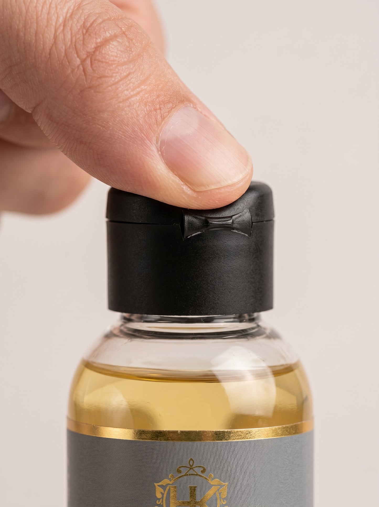 Hand holding a small bottle with a black cap against a neutral background
