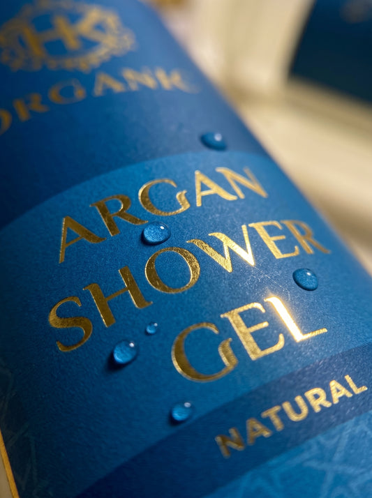 Blue bottle of Argan Shower Gel with gold text on a blurred background