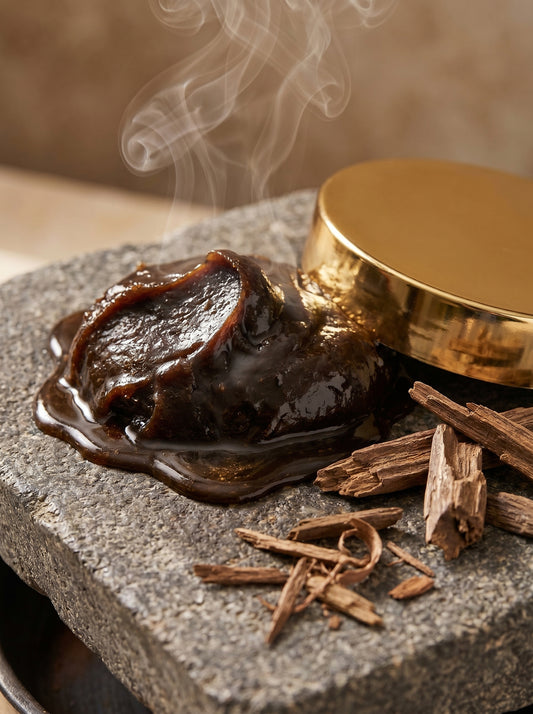 Smoldering incense stick on a stone surface with smoke rising, set against a neutral background.