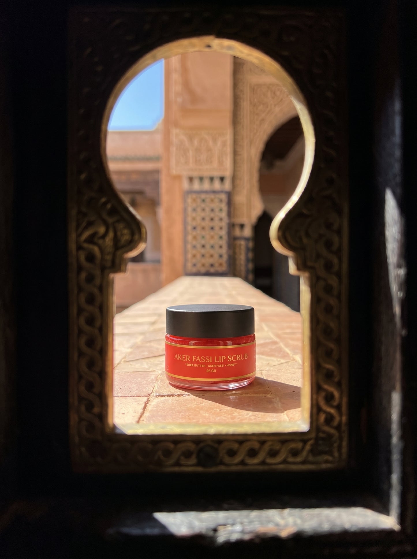 Red jar with black lid on a reflective surface, framed by an ornate mirror.