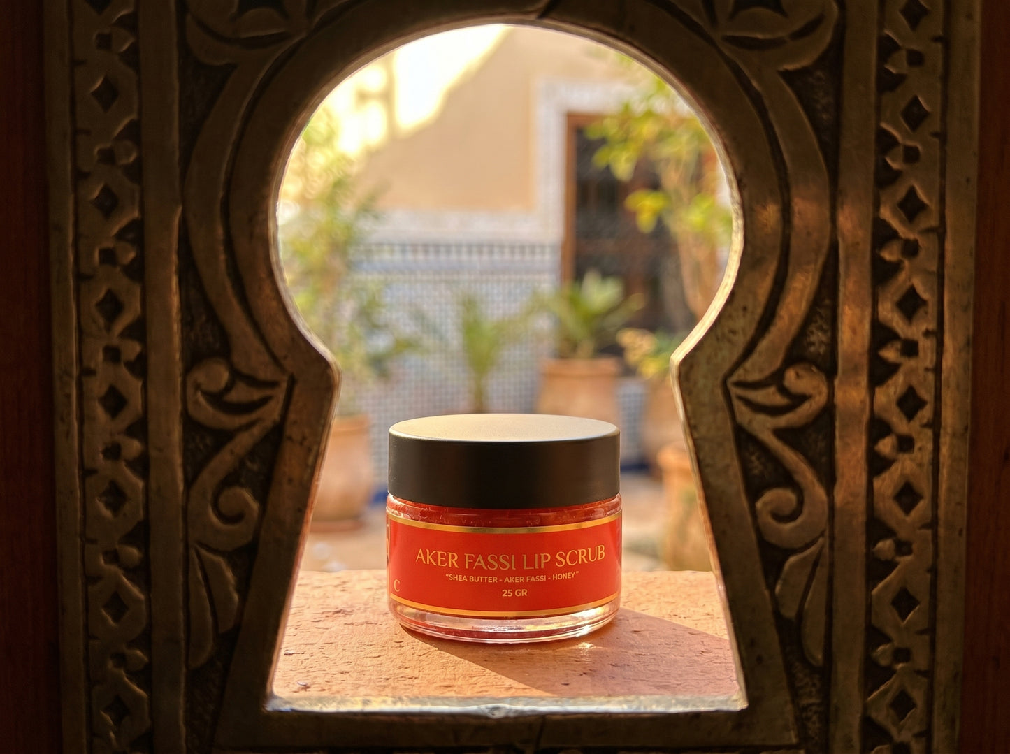 Jar of Aker Fassi Up Scrub in front of an ornate mirror with a blurred outdoor background