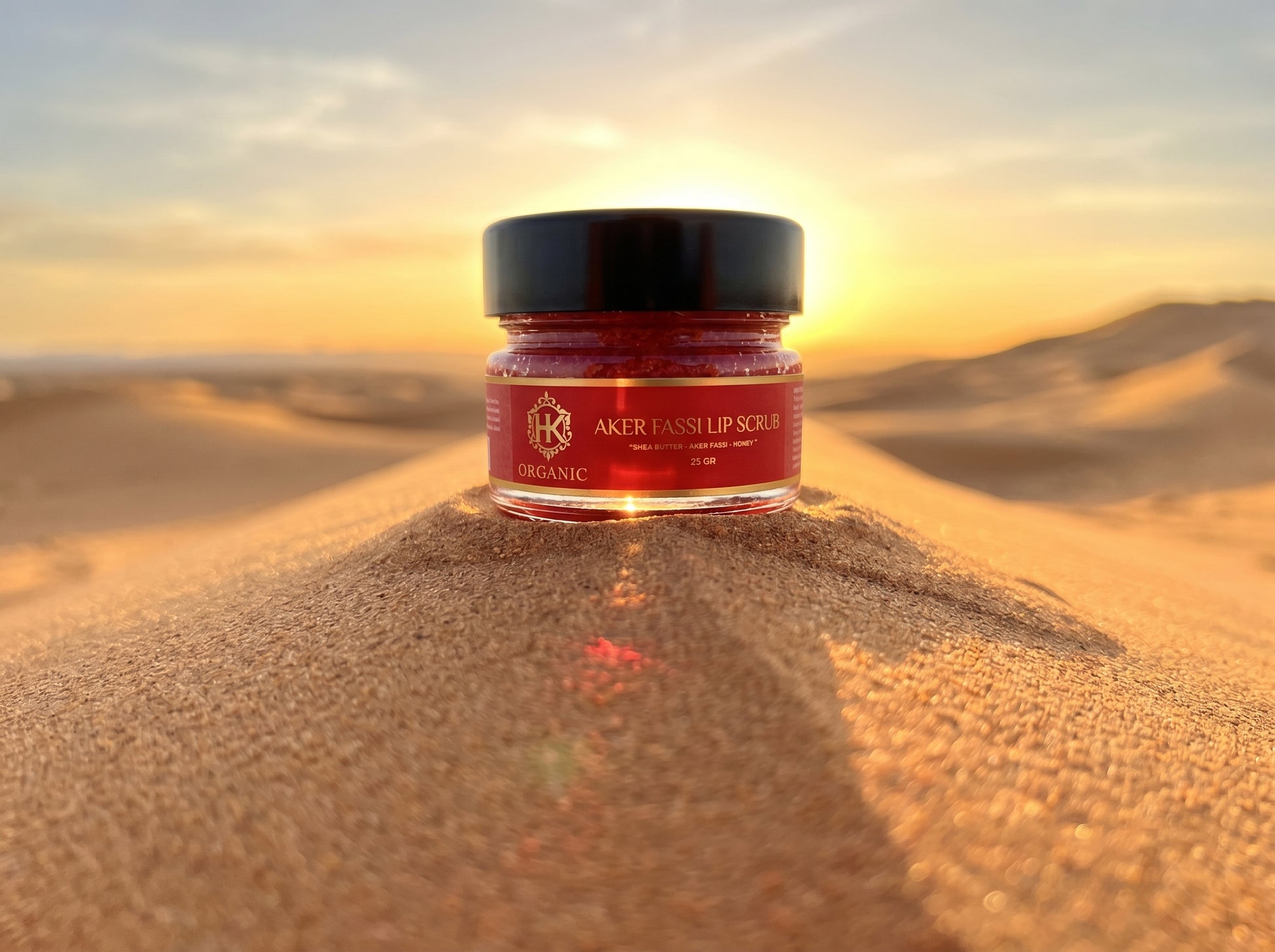 Jar of lip scrub on a sand dune with a sunset in the background