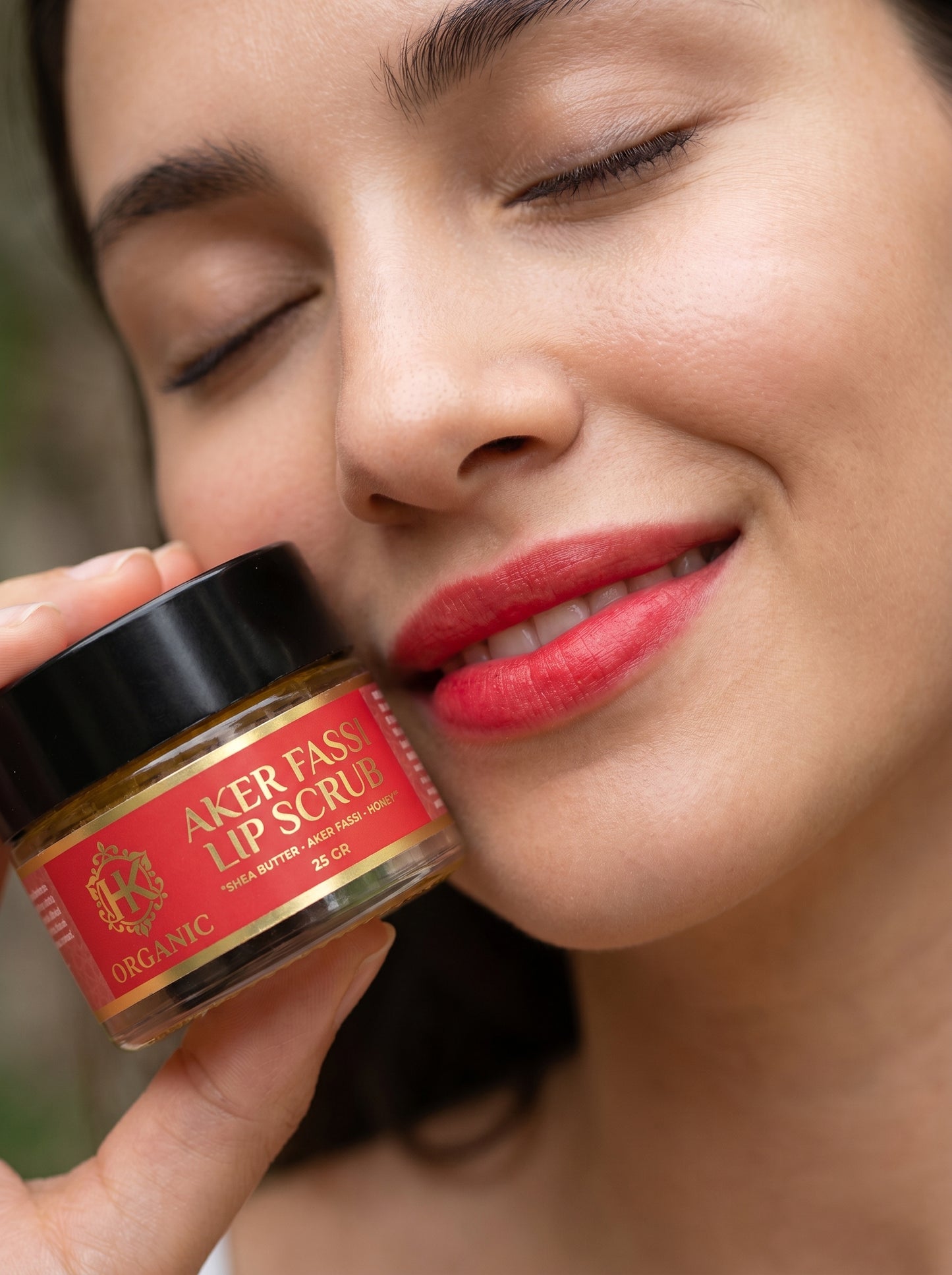 Woman holding Aker Fass lip scrub close to her lips with a blurred natural background