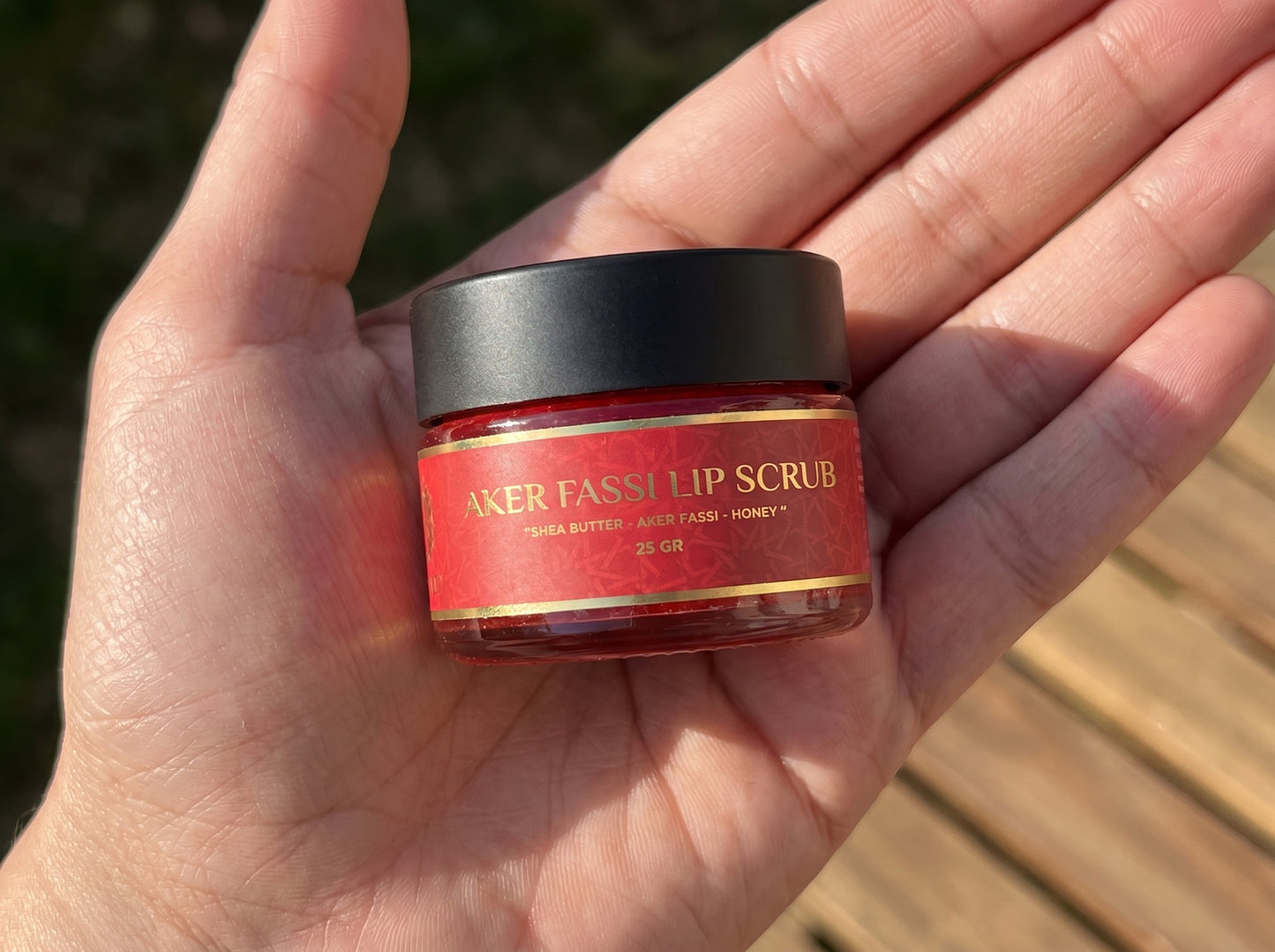 Hand holding a jar of Baker Fassh lip scrub with a red label.