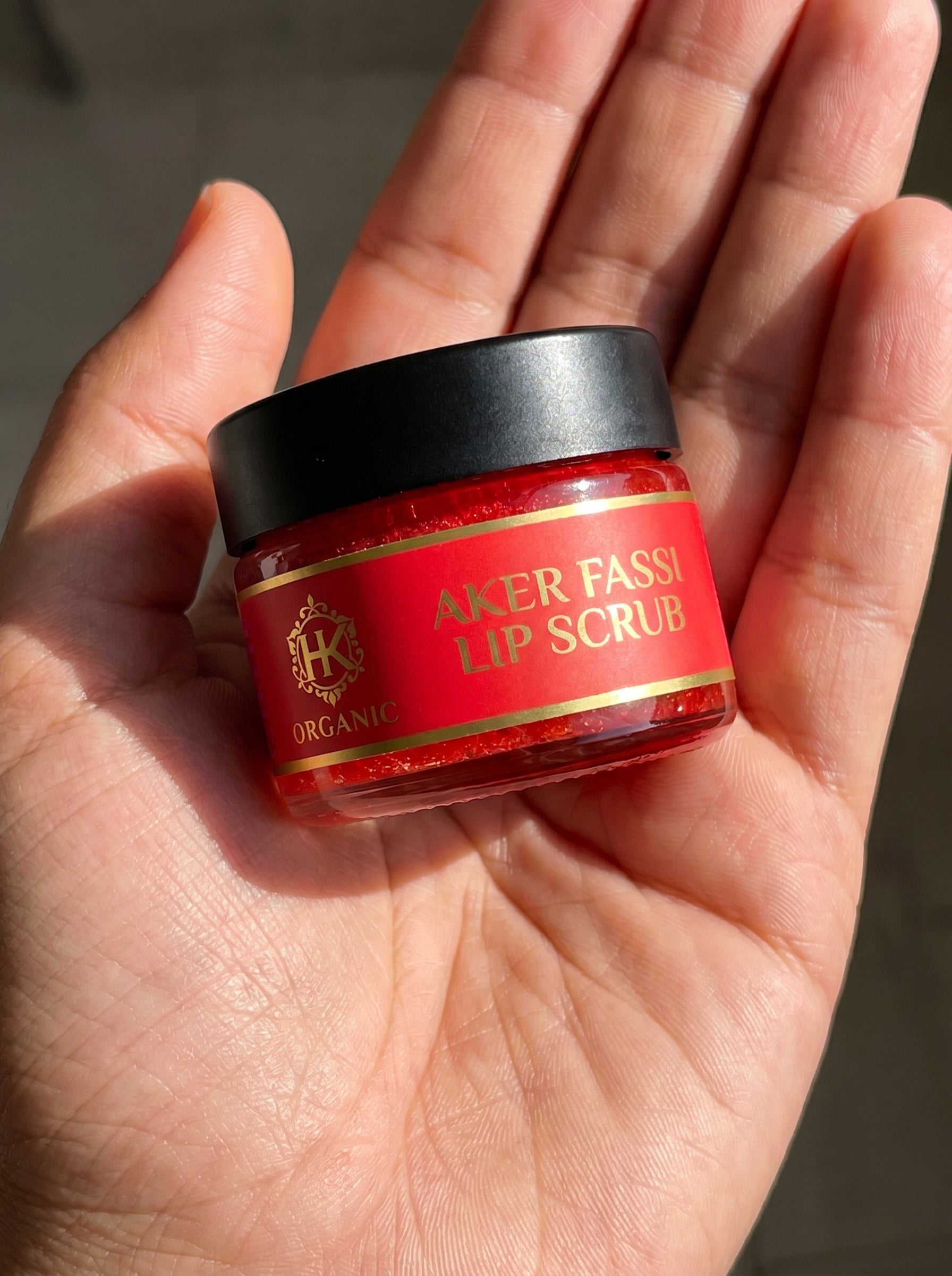 Hand holding a jar of Aker Fassi lip scrub with a red label.