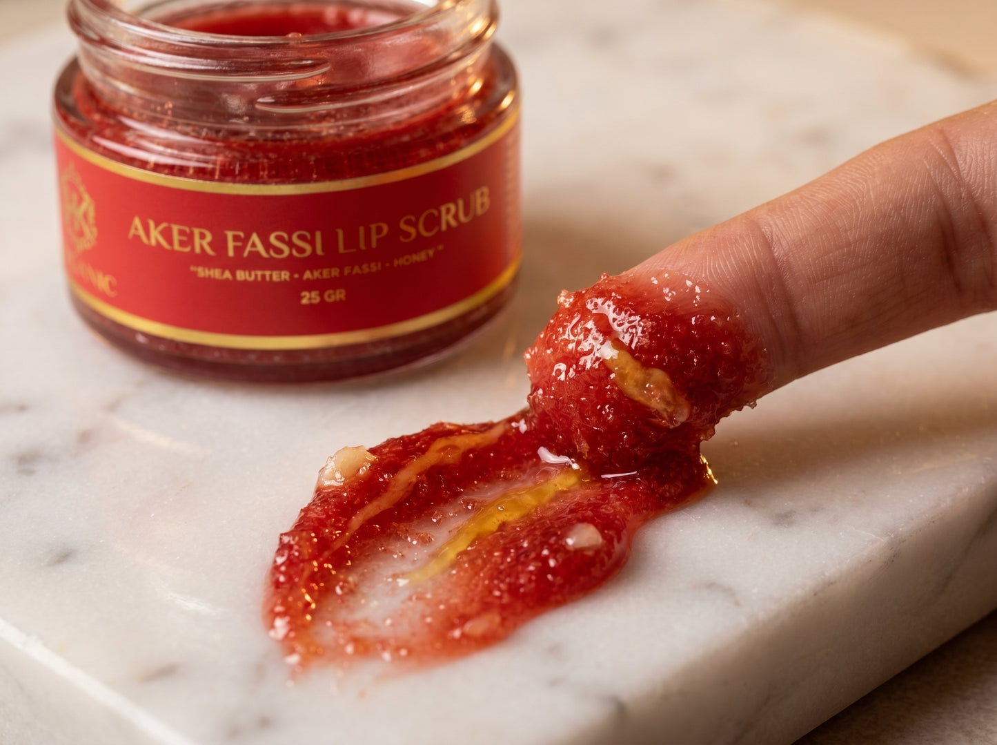Aker Fassi lip scrub with a finger applying it on a marble surface