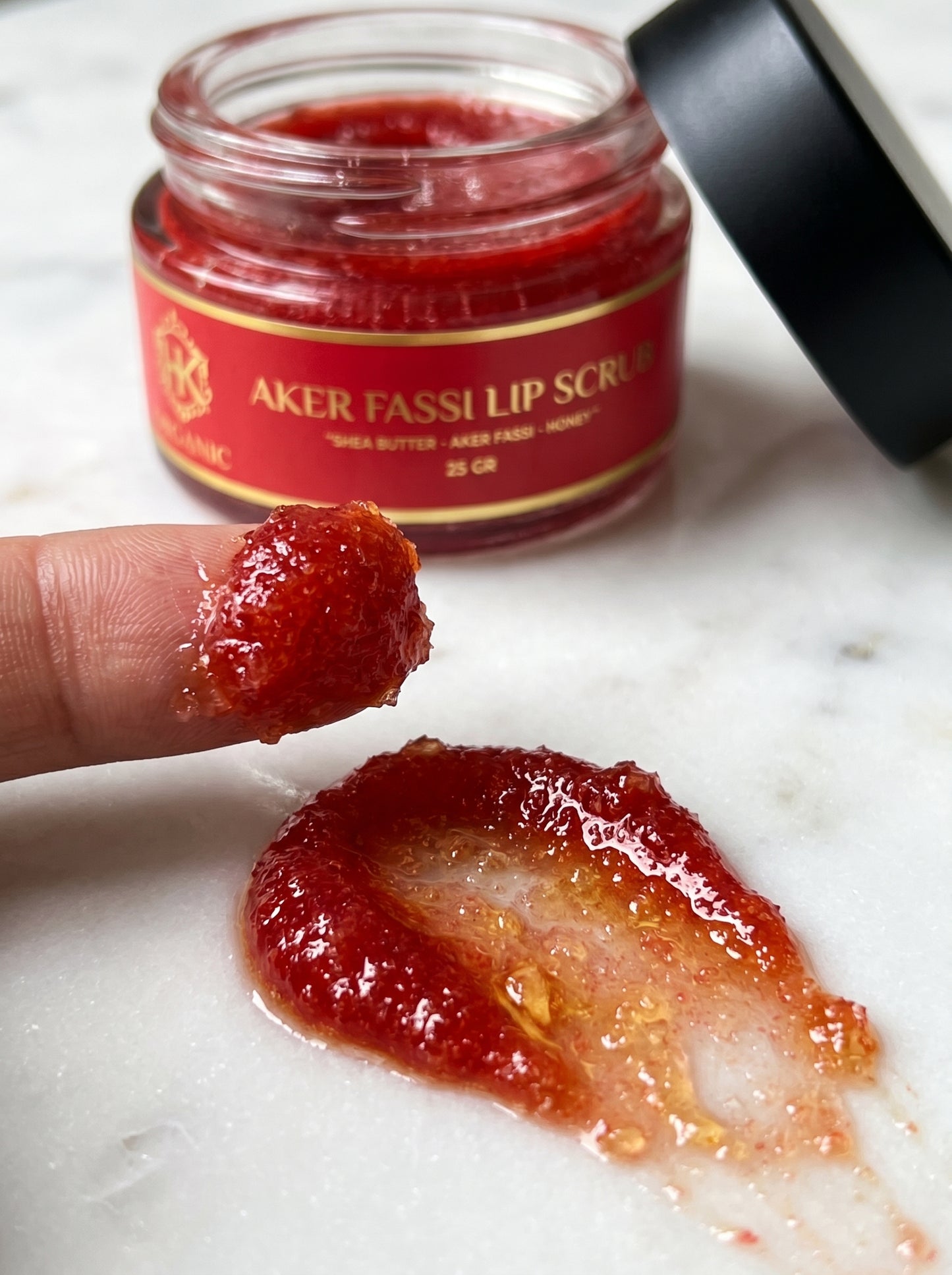 Jar of Aker Fasselip Scrub with a finger applying scrub to skin