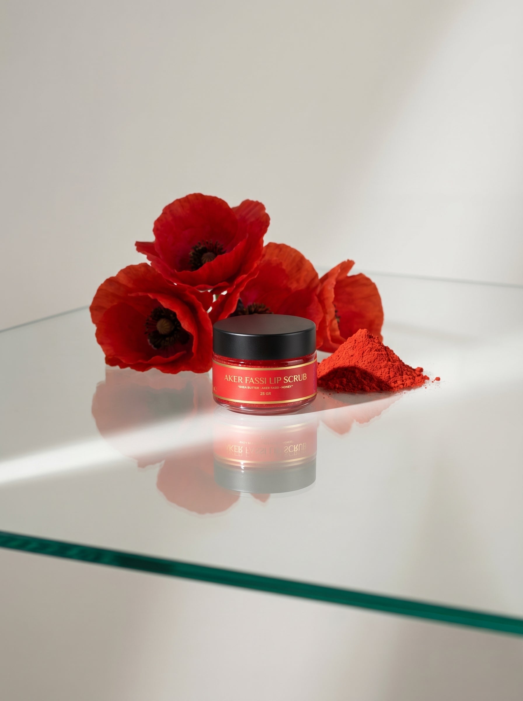 Red cosmetic jar with black lid on a reflective surface next to red flowers
