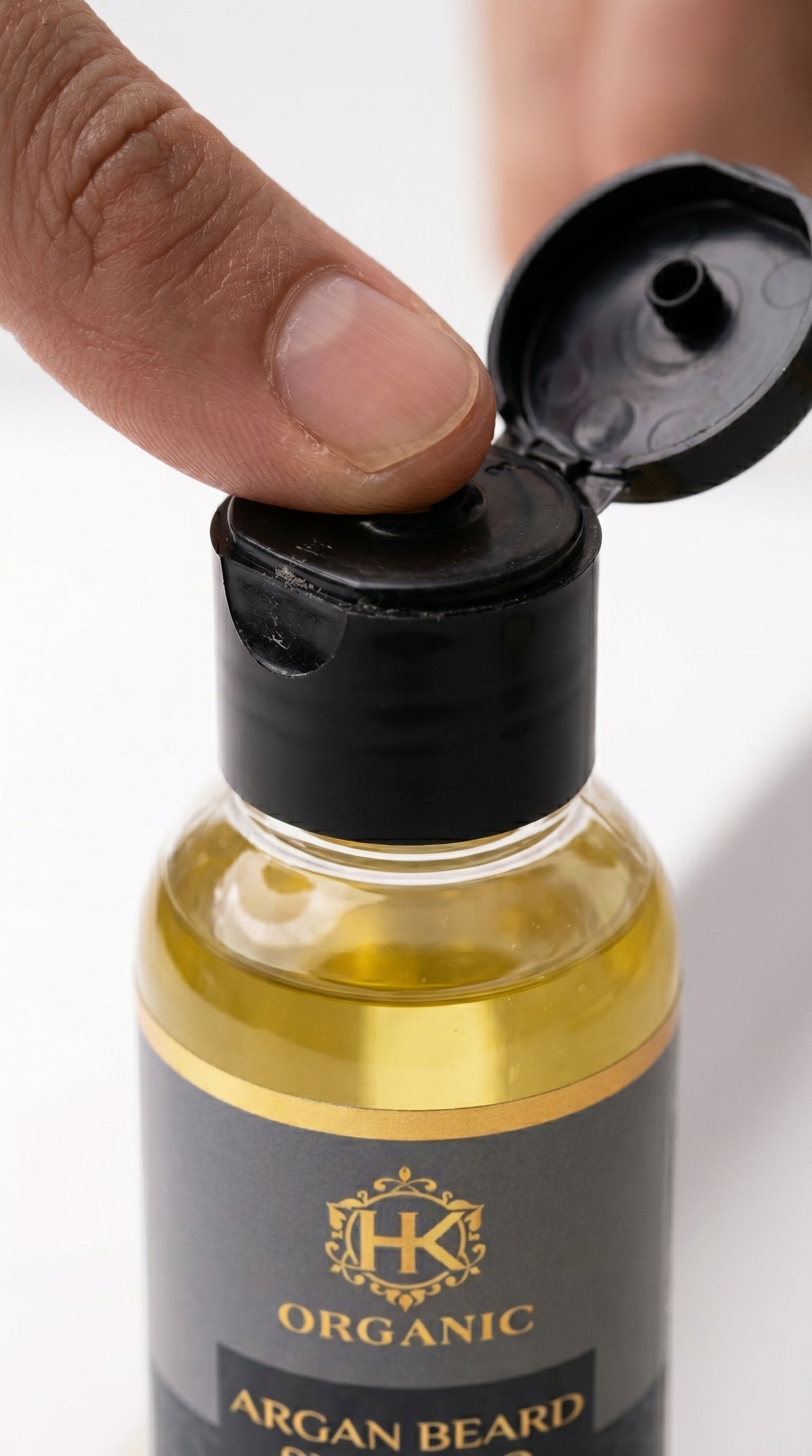 Bottle of organic argan beard oil with a hand opening the cap on a white background