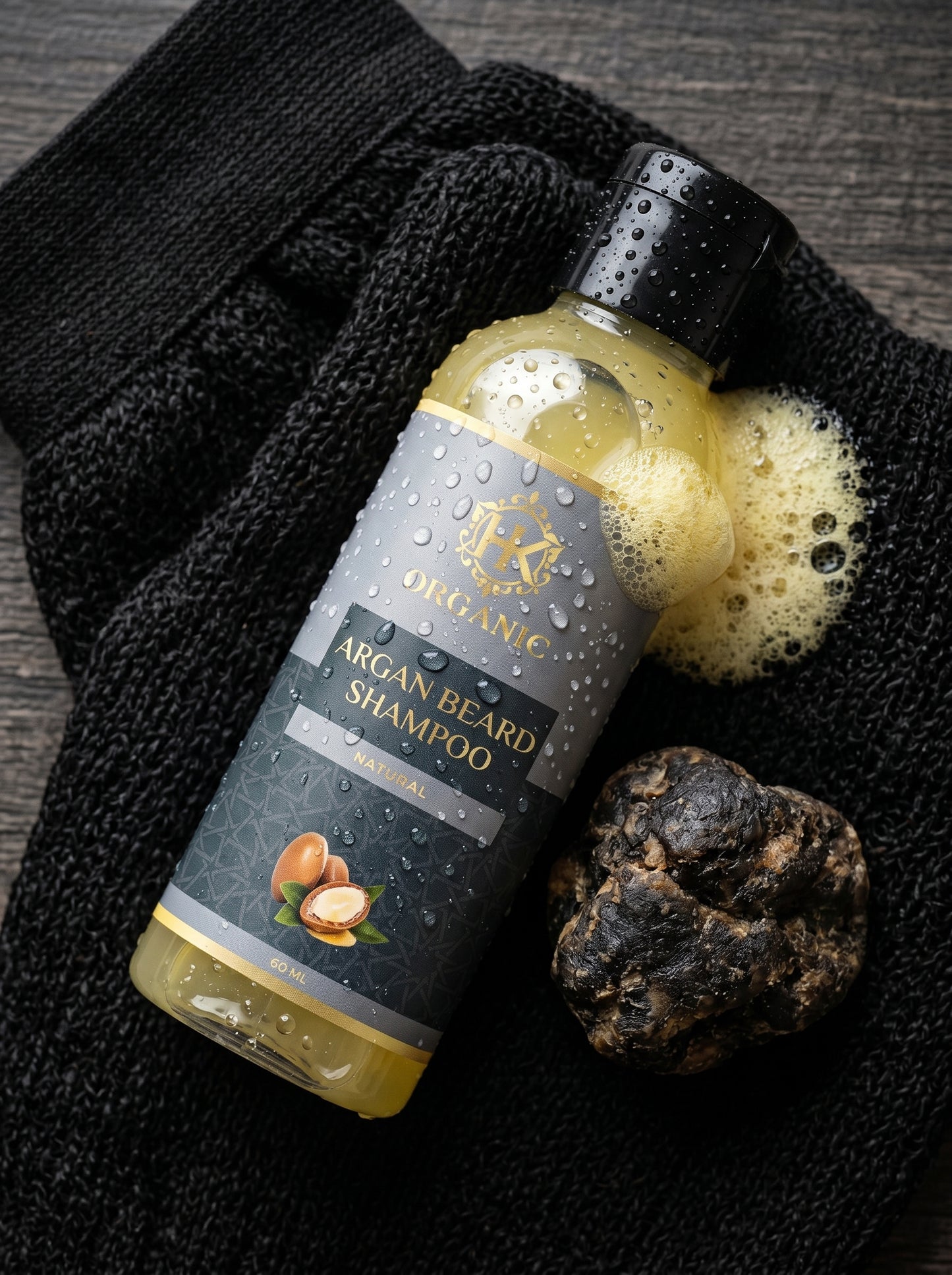 Bottle of Argan Beard Shampoo with a black towel and a sponge on a dark surface