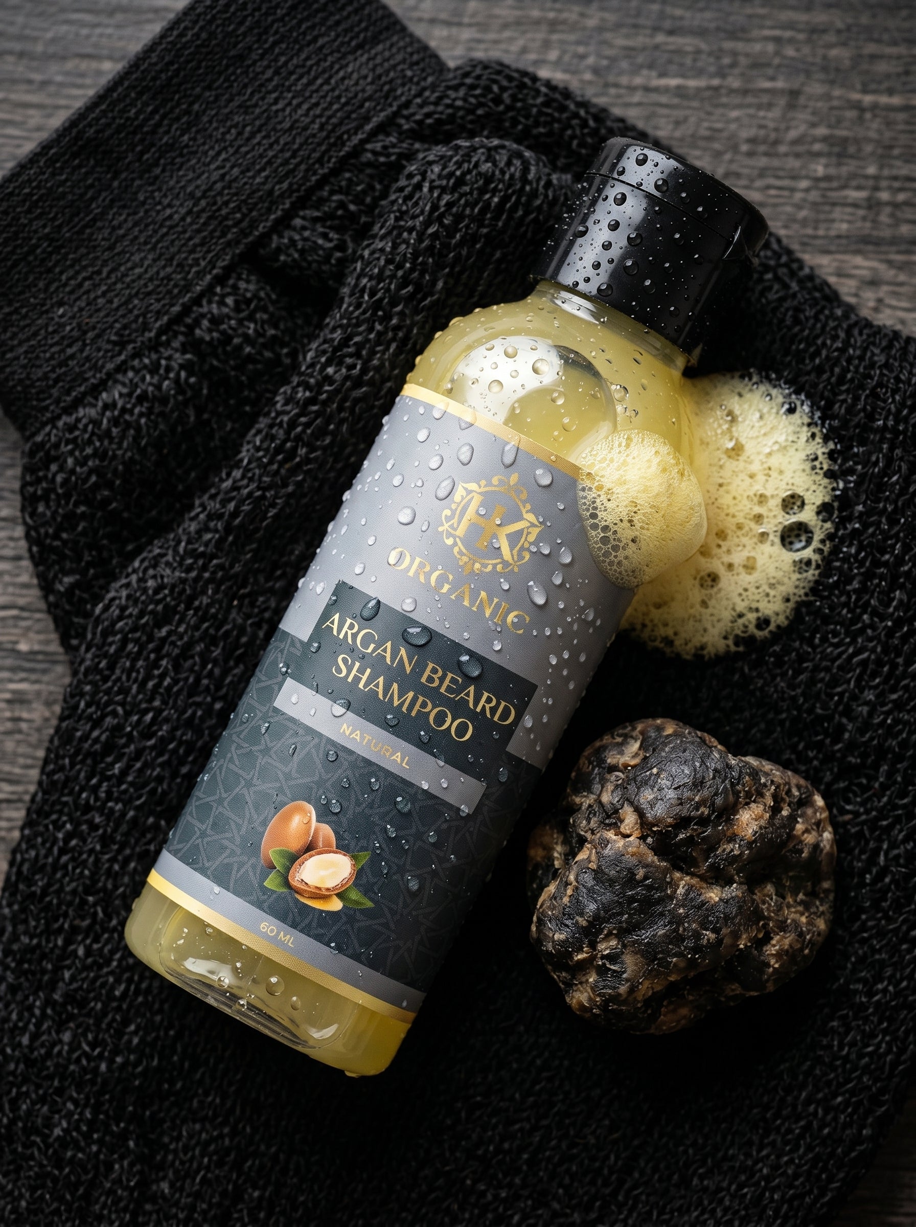 Bottle of Argan Beard Shampoo with a black towel and a sponge on a dark surface