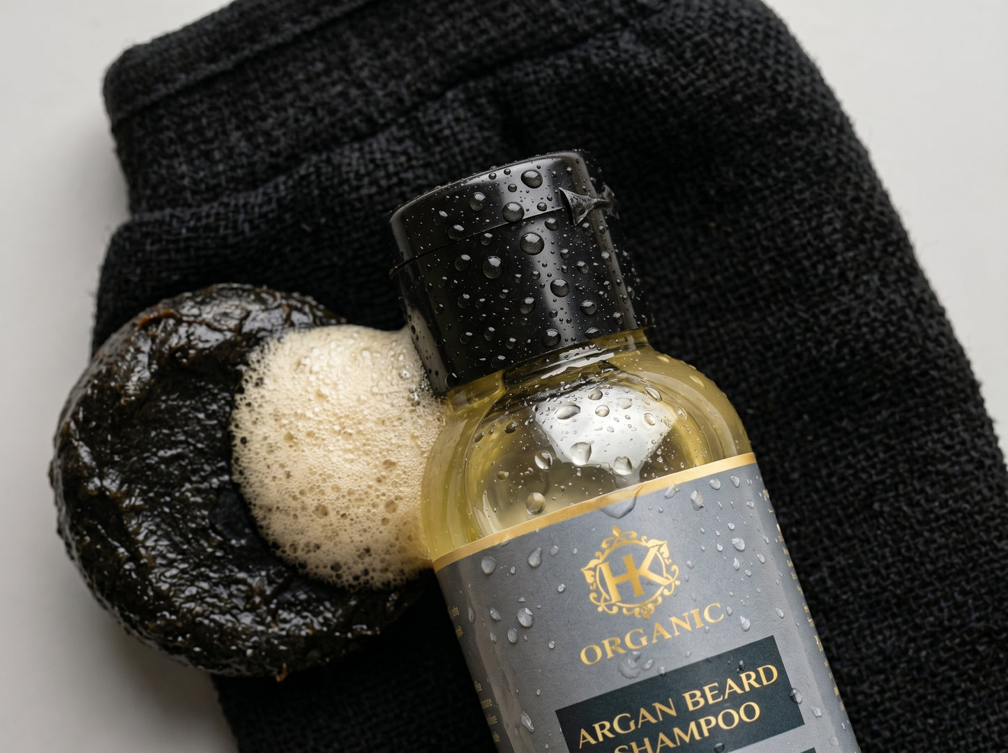 Bottle of Organic Argan Beard Shampoo with a loofah and towel on a neutral background