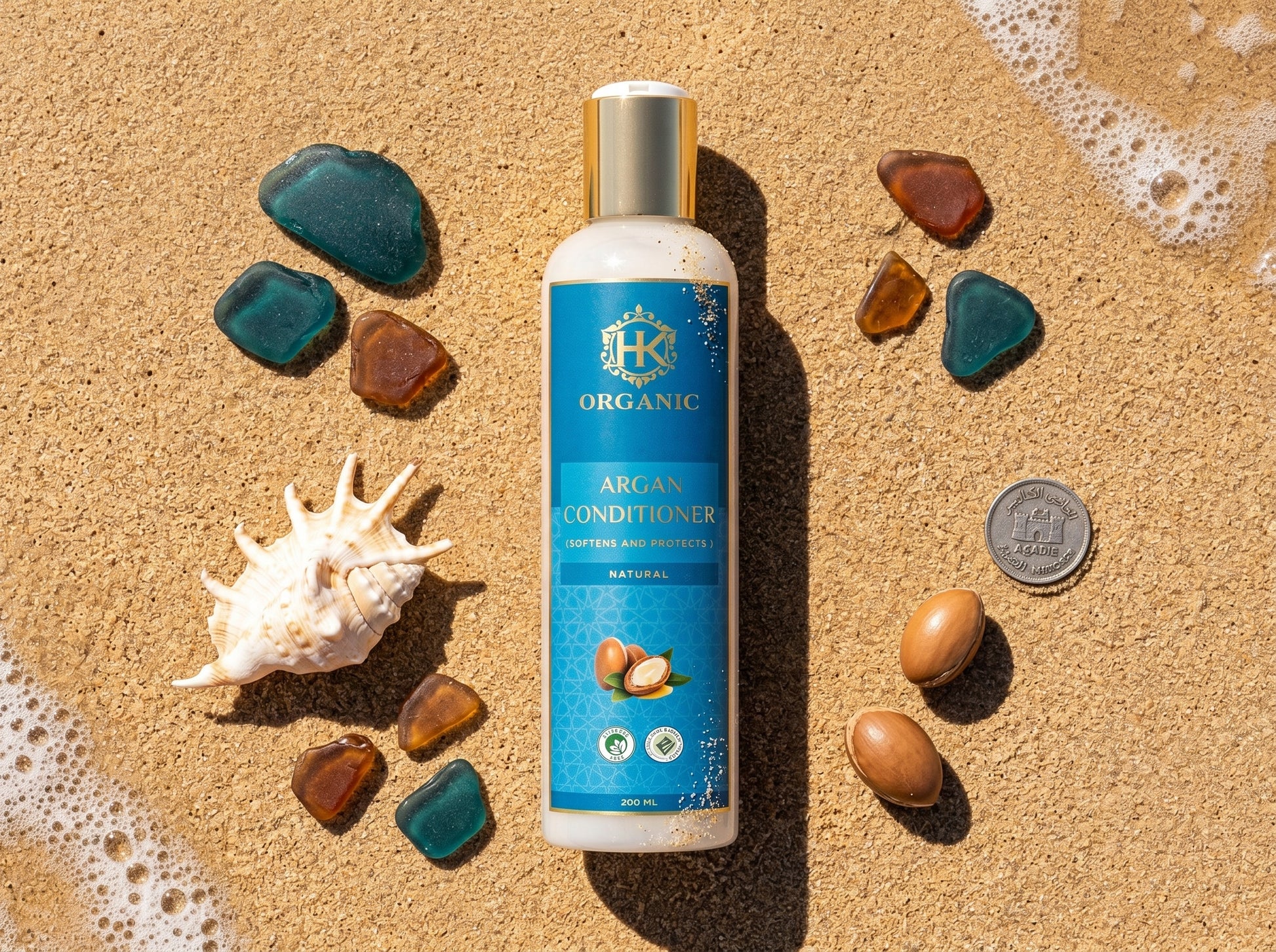 Bottle of organic argan conditioner on a sandy background with seashells and stones.