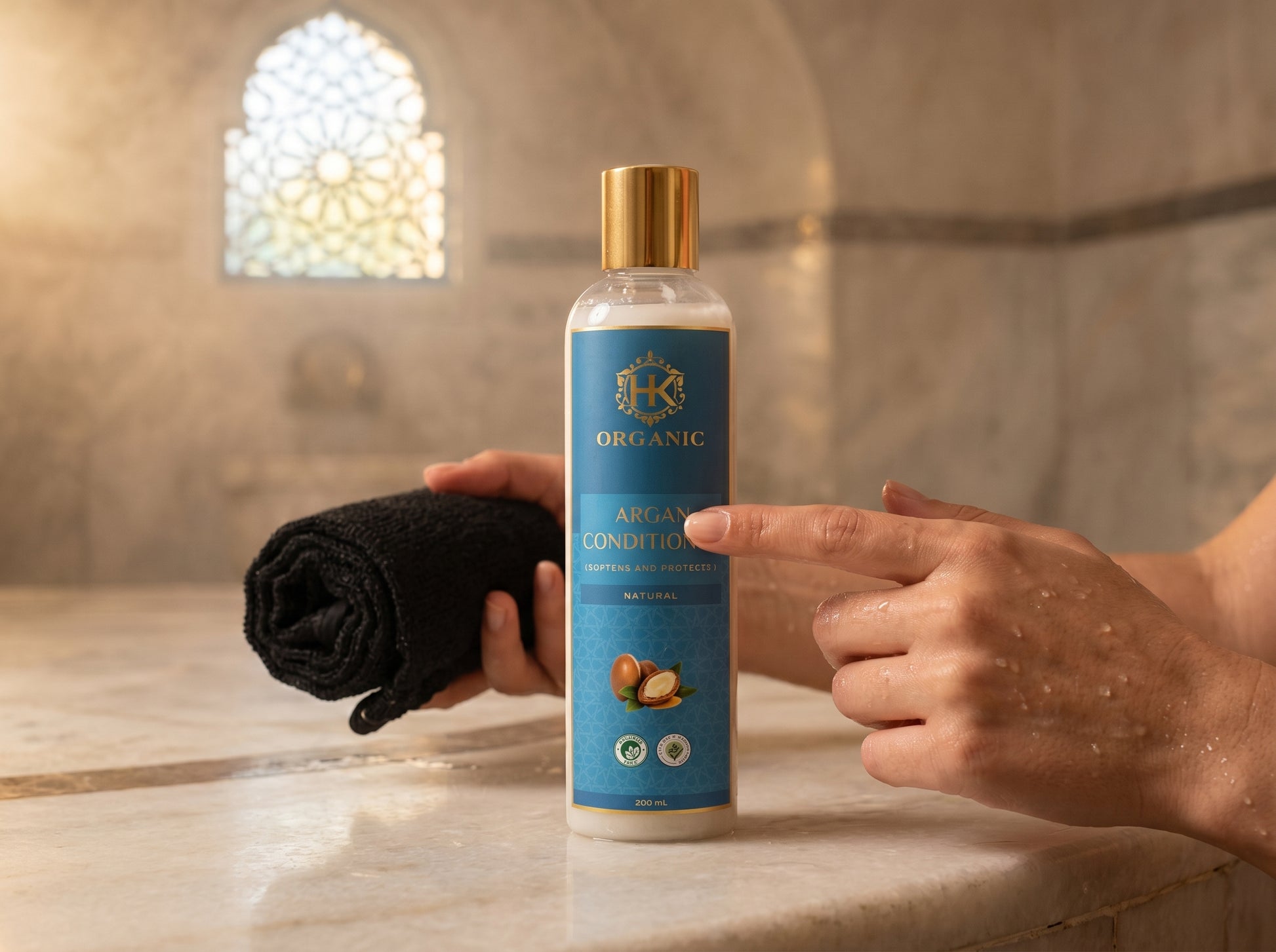 Person holding a bottle of organic shower gel with a black towel in a bathroom setting