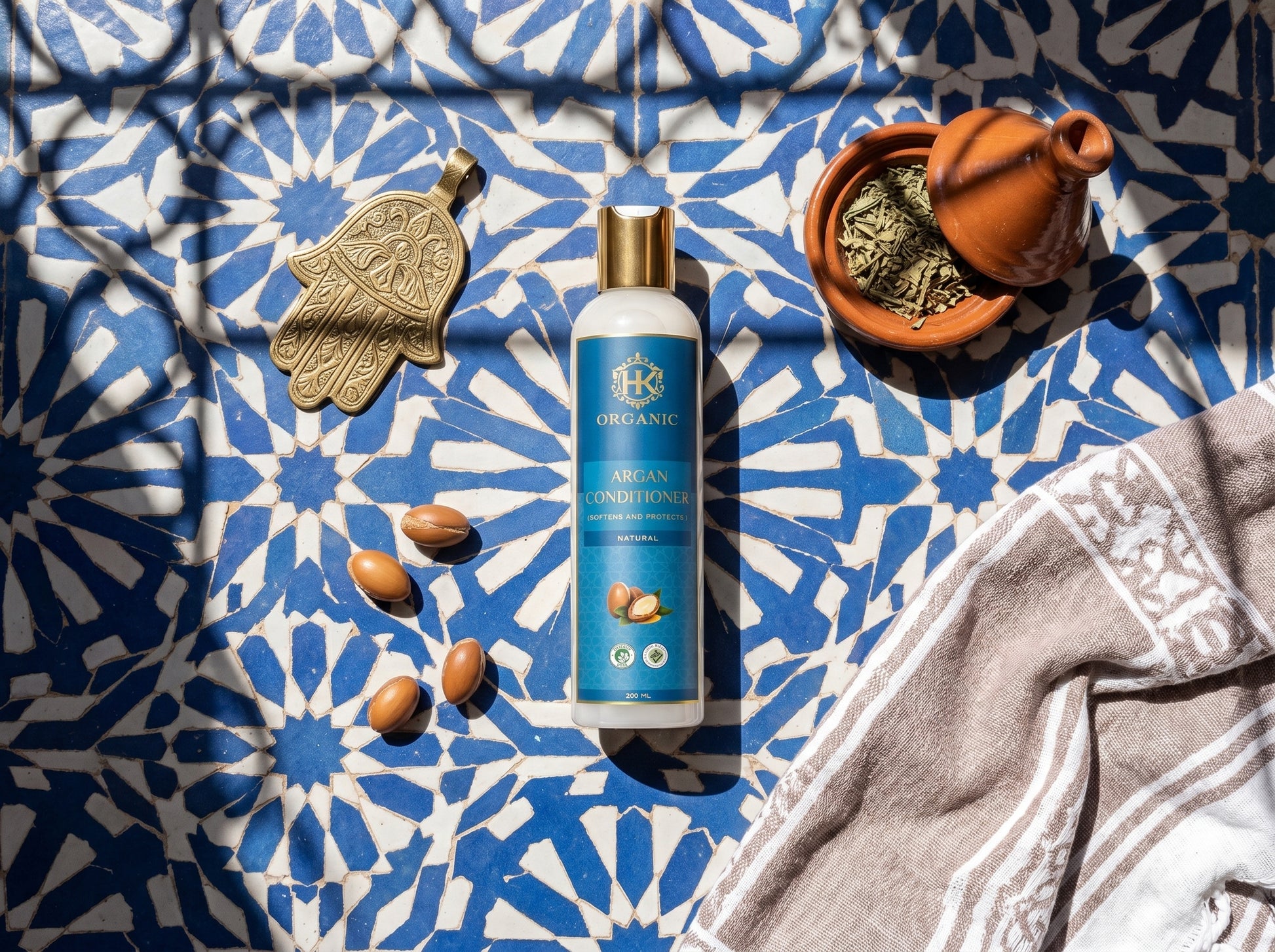 Blue bottle of organic conditioner on a blue and white patterned fabric with herbs and a towel.