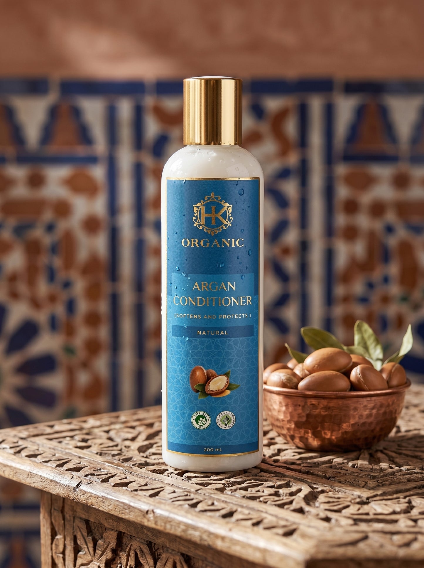 Bottle of organic argan conditioner on a wooden table with a bowl of argan nuts and a patterned wall in the background.