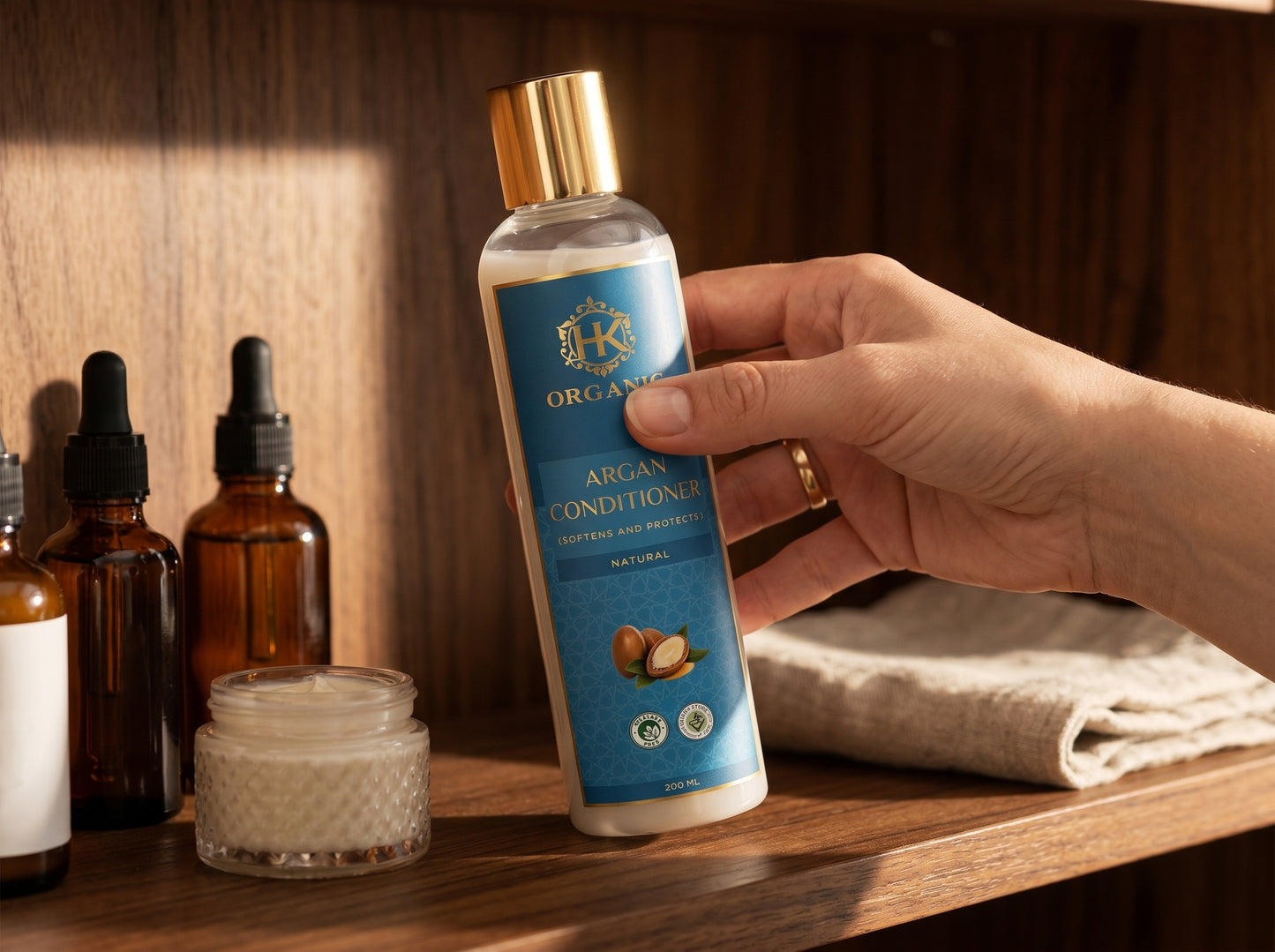 Hand holding a bottle of HK Organics Argan Conditioner on a wooden surface with other skincare products.