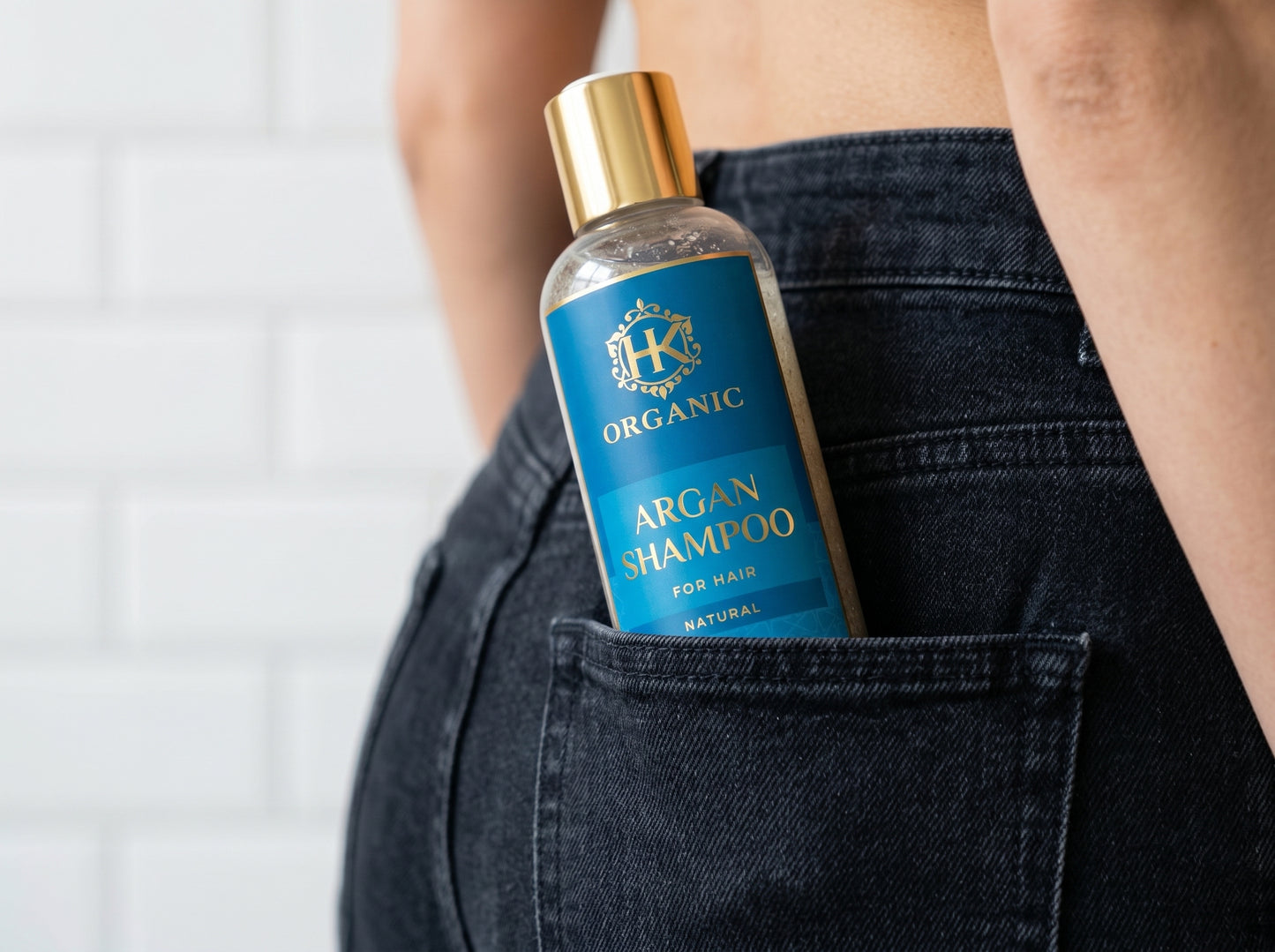 Bottle of organic argan shampoo held in a person's pocket against a white background