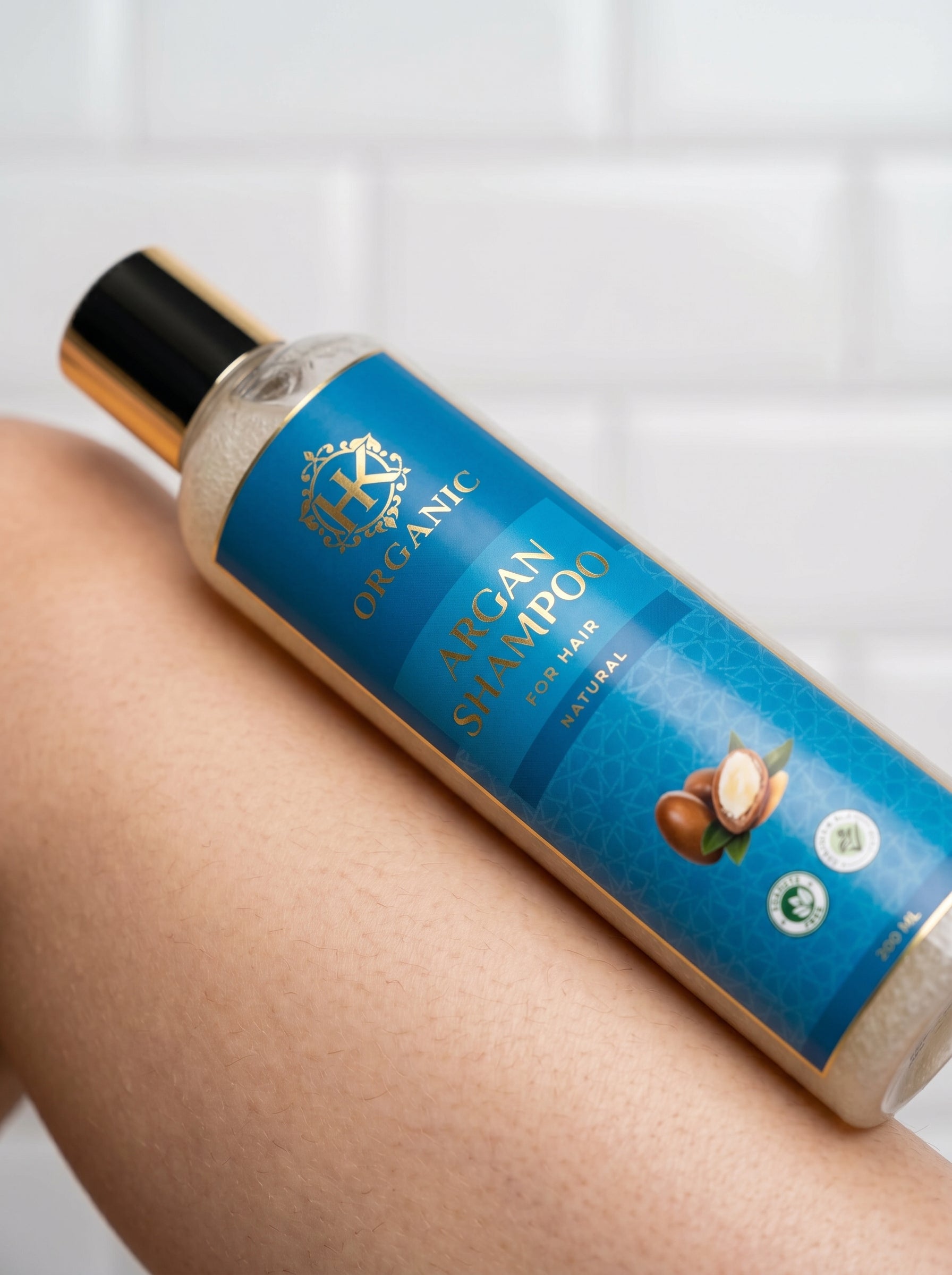 Bottle of organic argan shampoo on a person's arm with a white tiled background