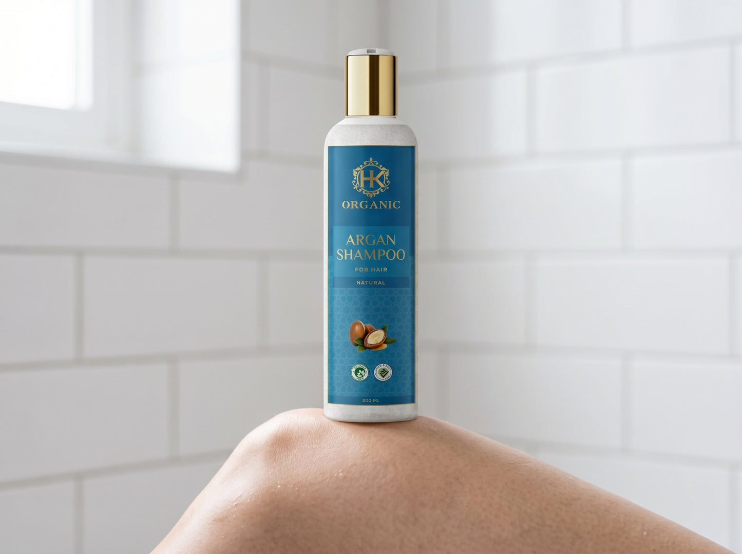 Bottle of Organic Argan Shampoo held by a person against a tiled bathroom wall.