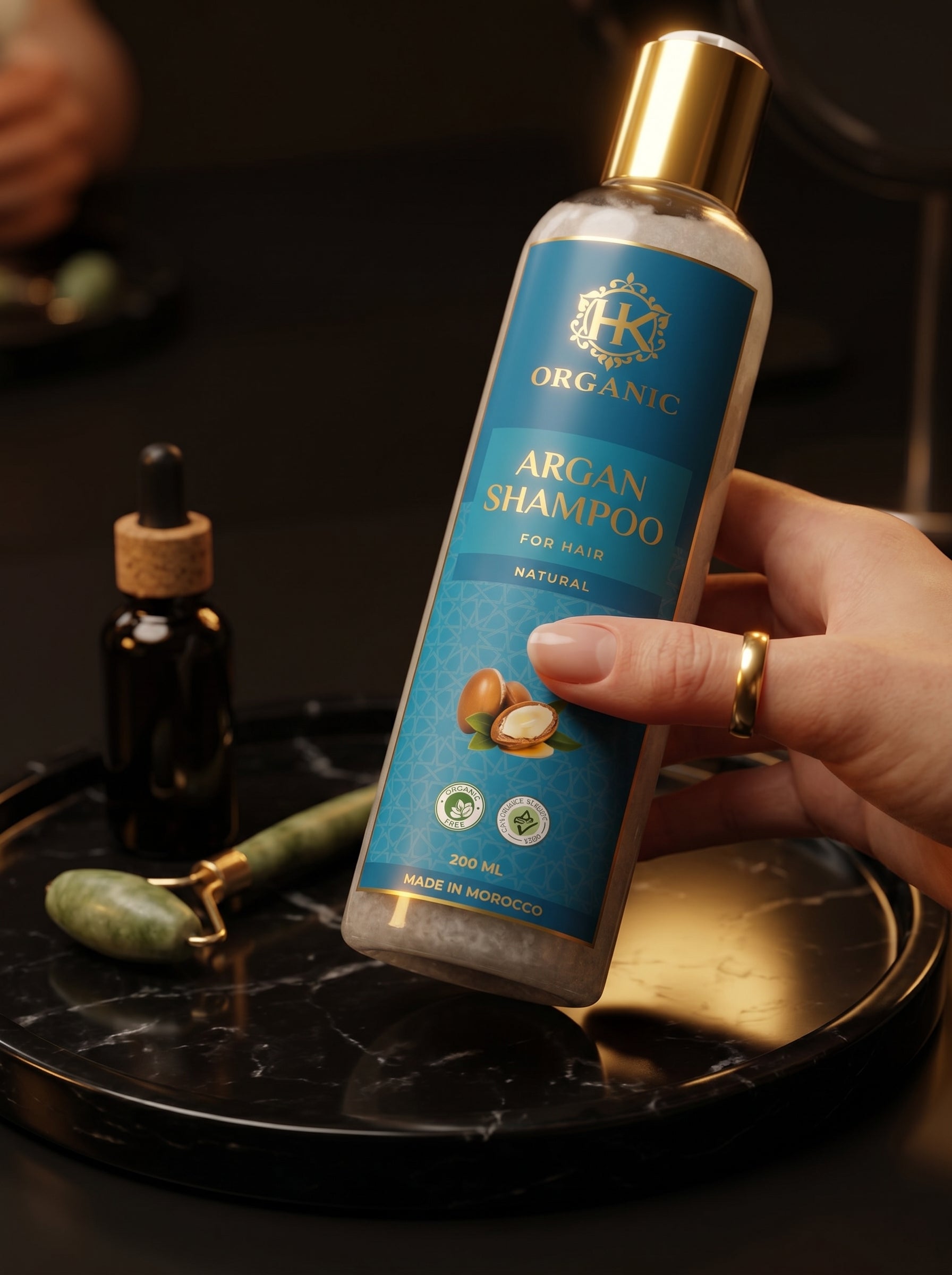 Hand holding a bottle of argan shampoo on a dark surface with a blurred background