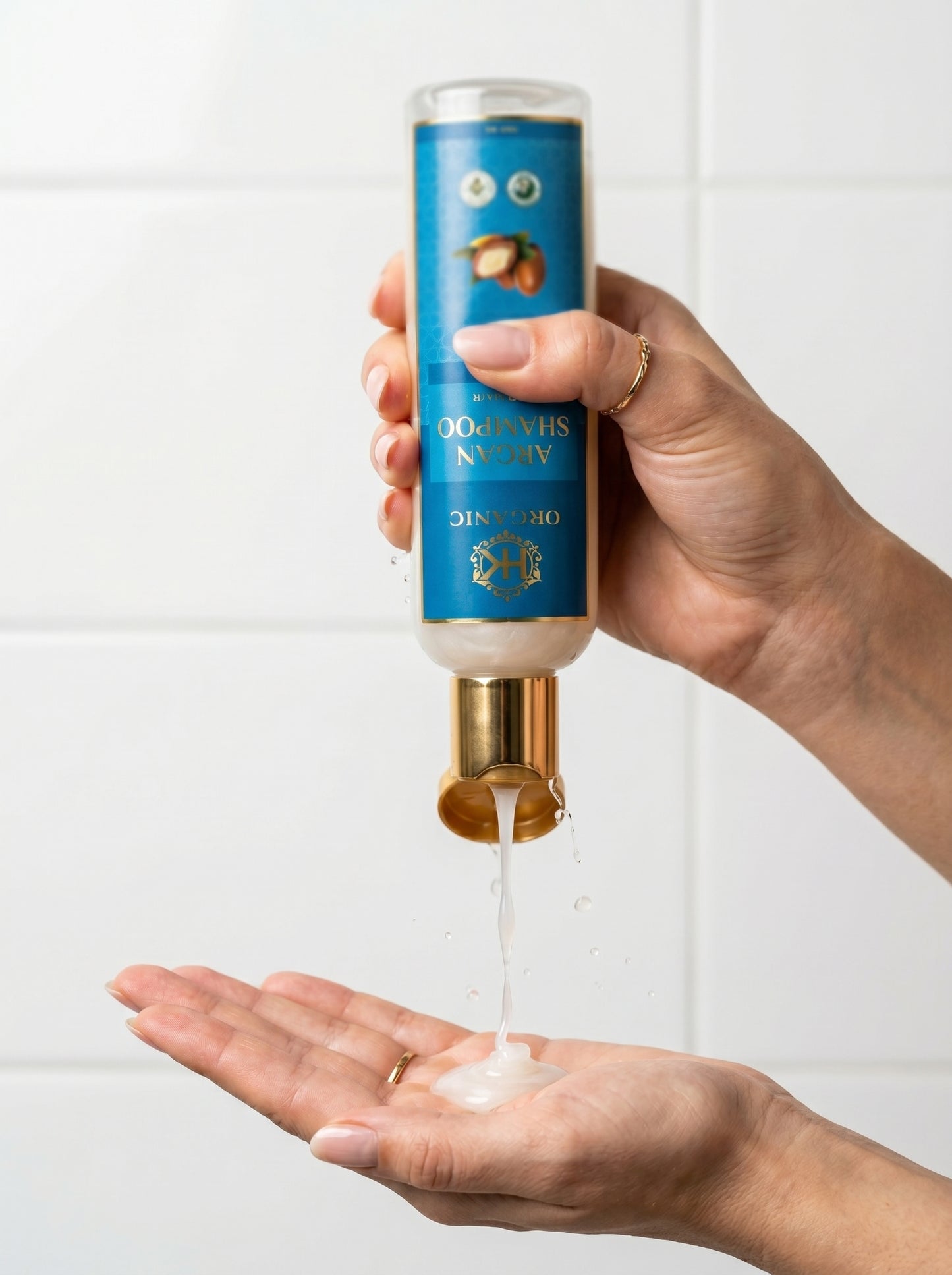 Hand holding a blue and gold bottle with a white liquid being poured onto a palm against a white background.