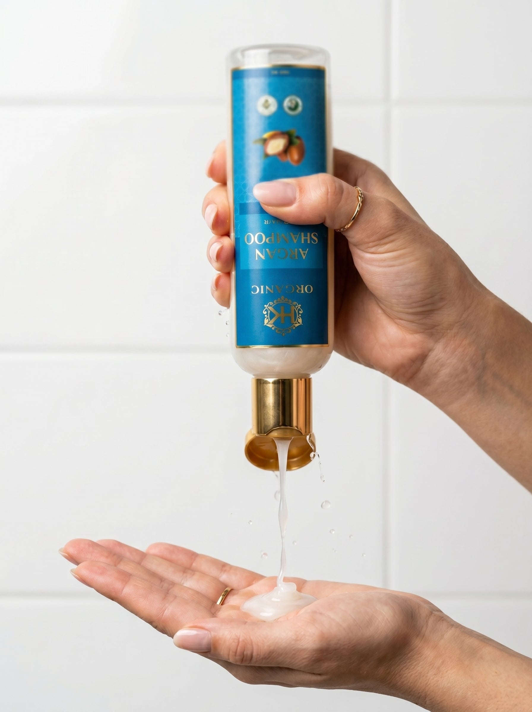 Hand holding a blue and gold bottle with a white liquid being poured onto a palm against a white background.
