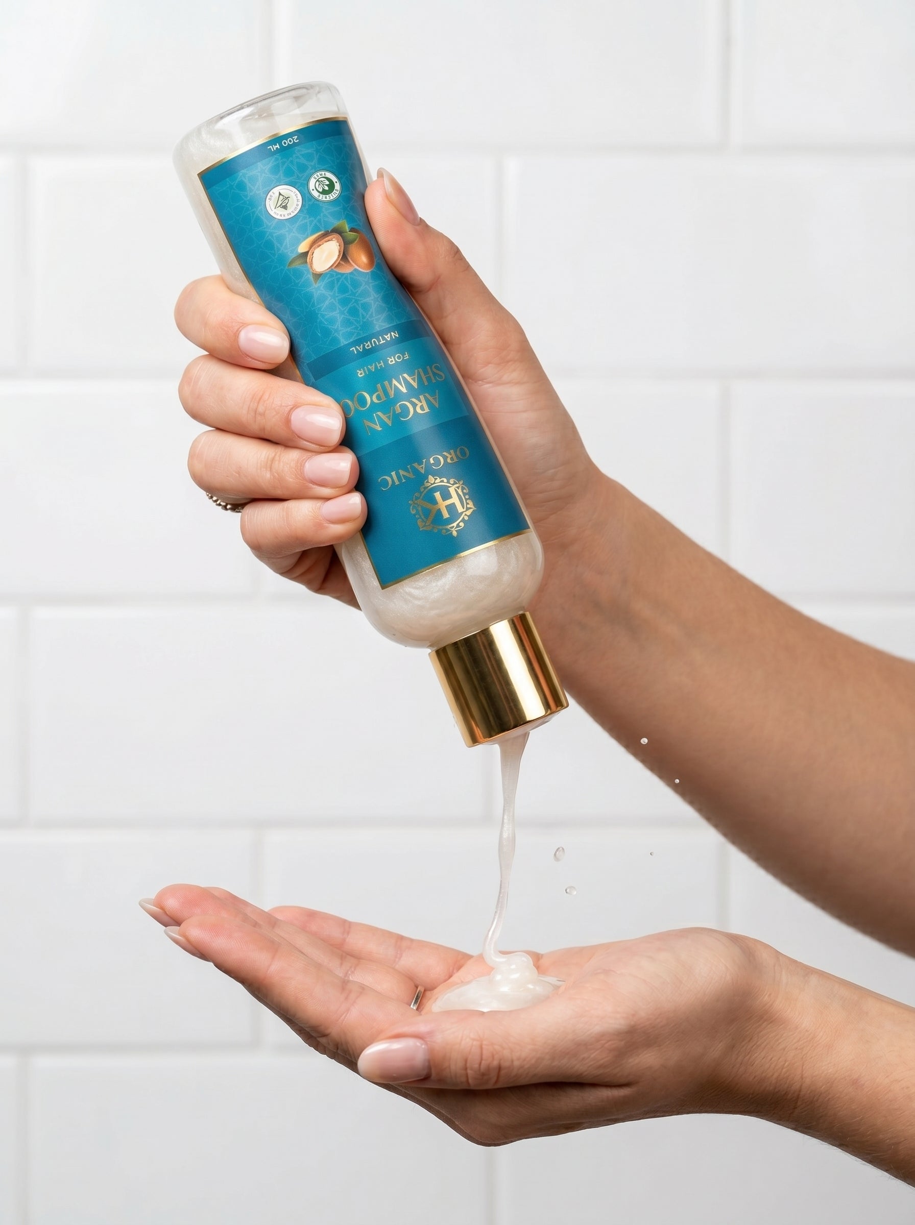 Hand holding a blue bottle of shampoo with white foam being dispensed onto a palm against a tiled wall background.