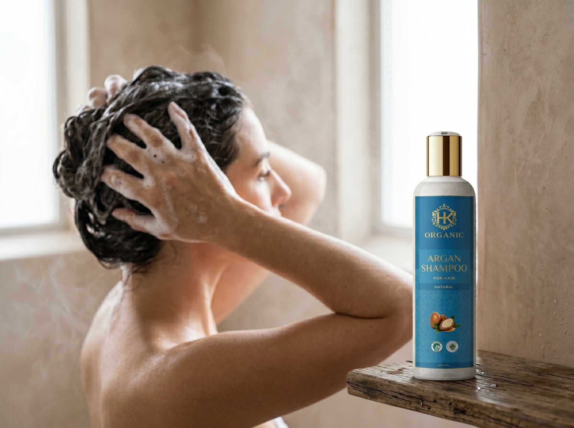 Person washing hair with a bottle of organic argan shampoo on a wooden shelf.