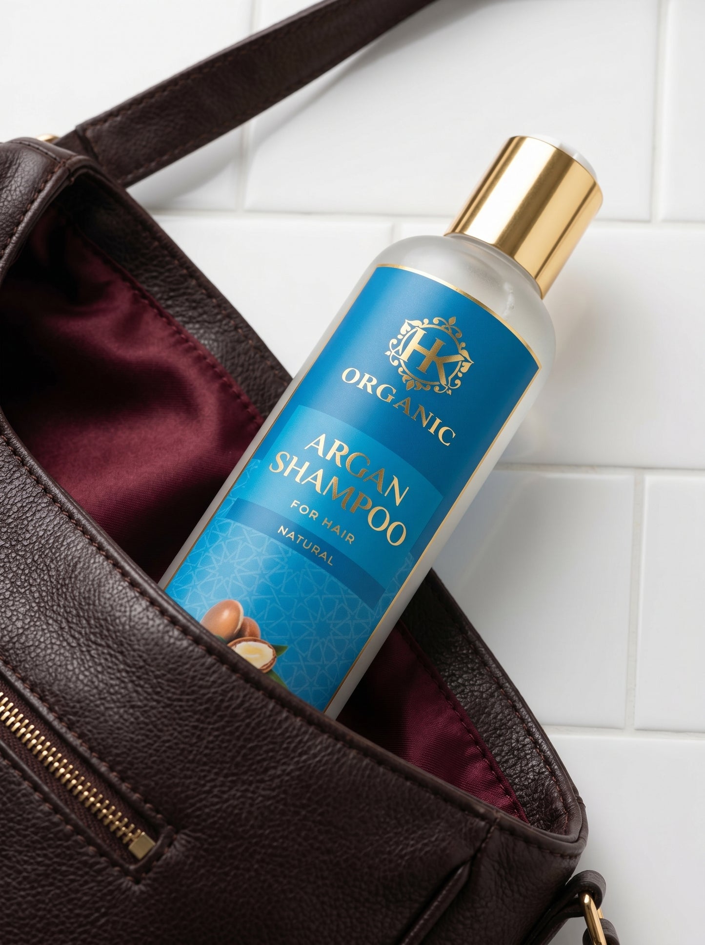 Shampoo bottle labeled 'Organic Argan Shampoo' inside a brown leather bag on a white tiled floor.