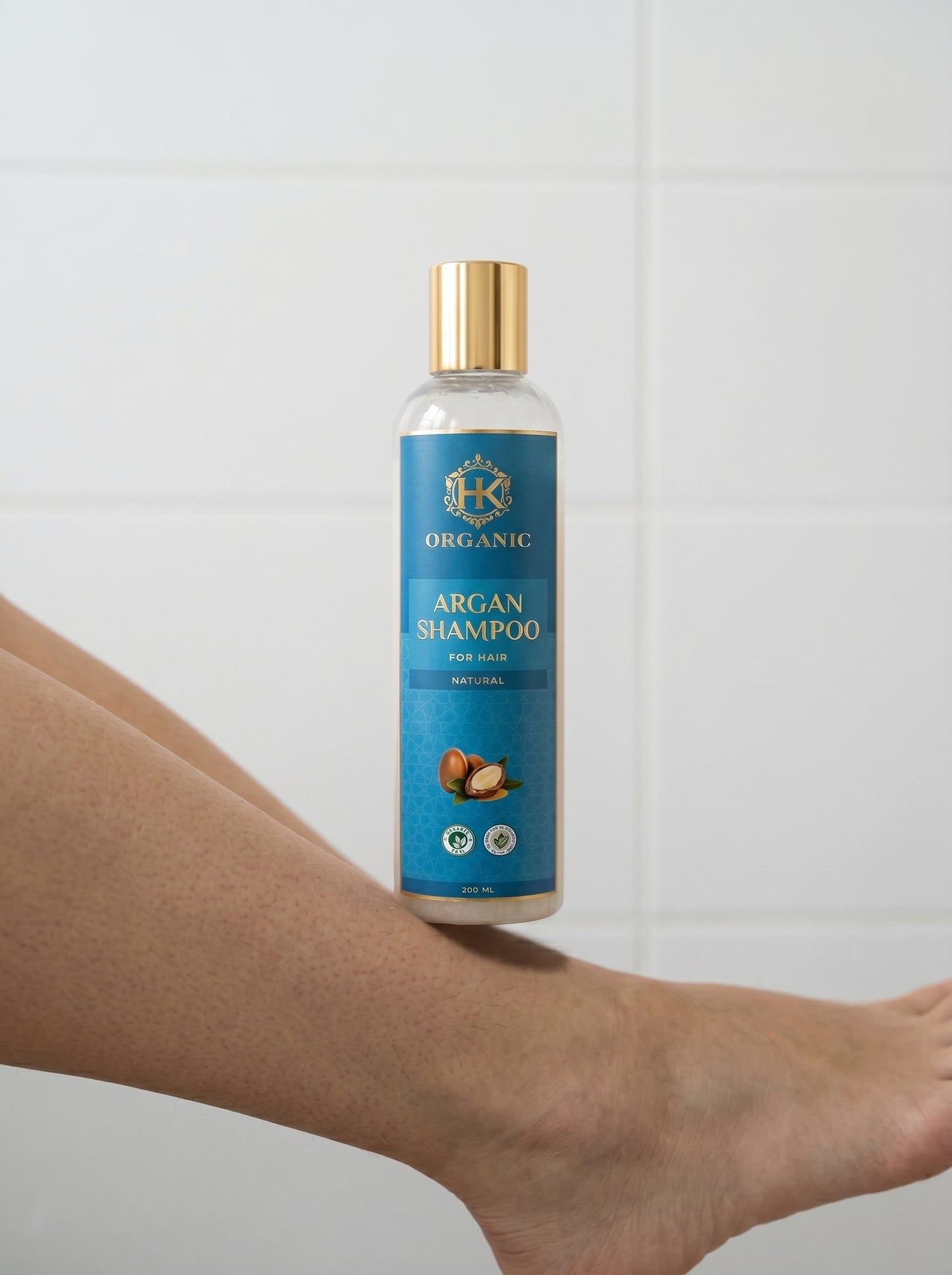 Bottle of organic argan shampoo held by a person against a white tiled wall.