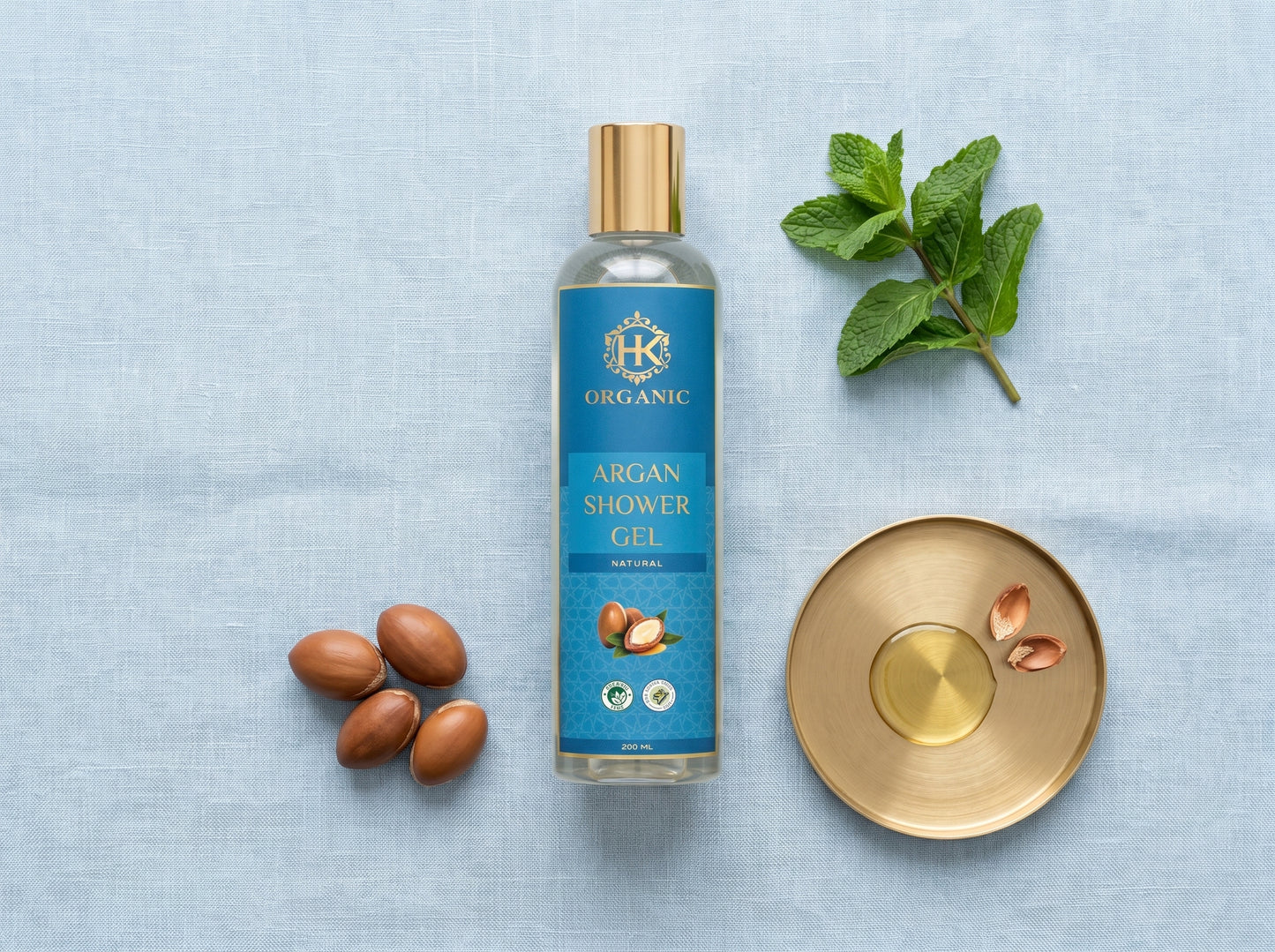 Bottle of argan shower gel with argan seeds and a leaf on a light blue background