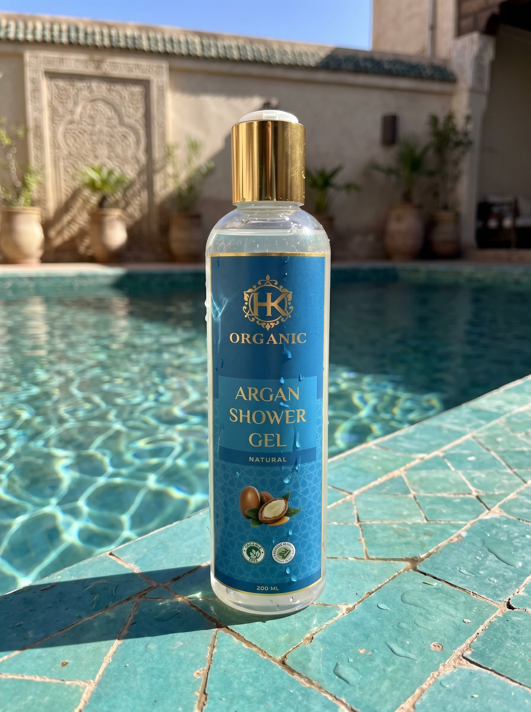 Bottle of Organic Argan Shower Gel on a poolside with decorative wall and plants in the background