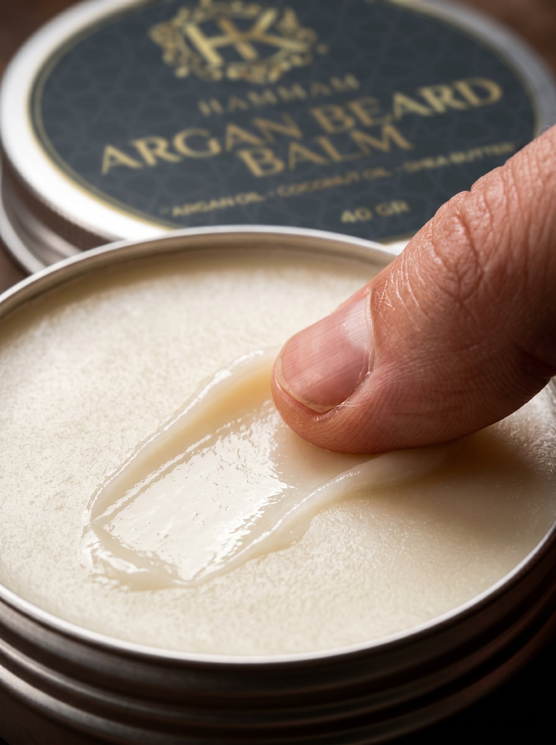 Hand applying argan beard balm from a container with a visible brand logo.