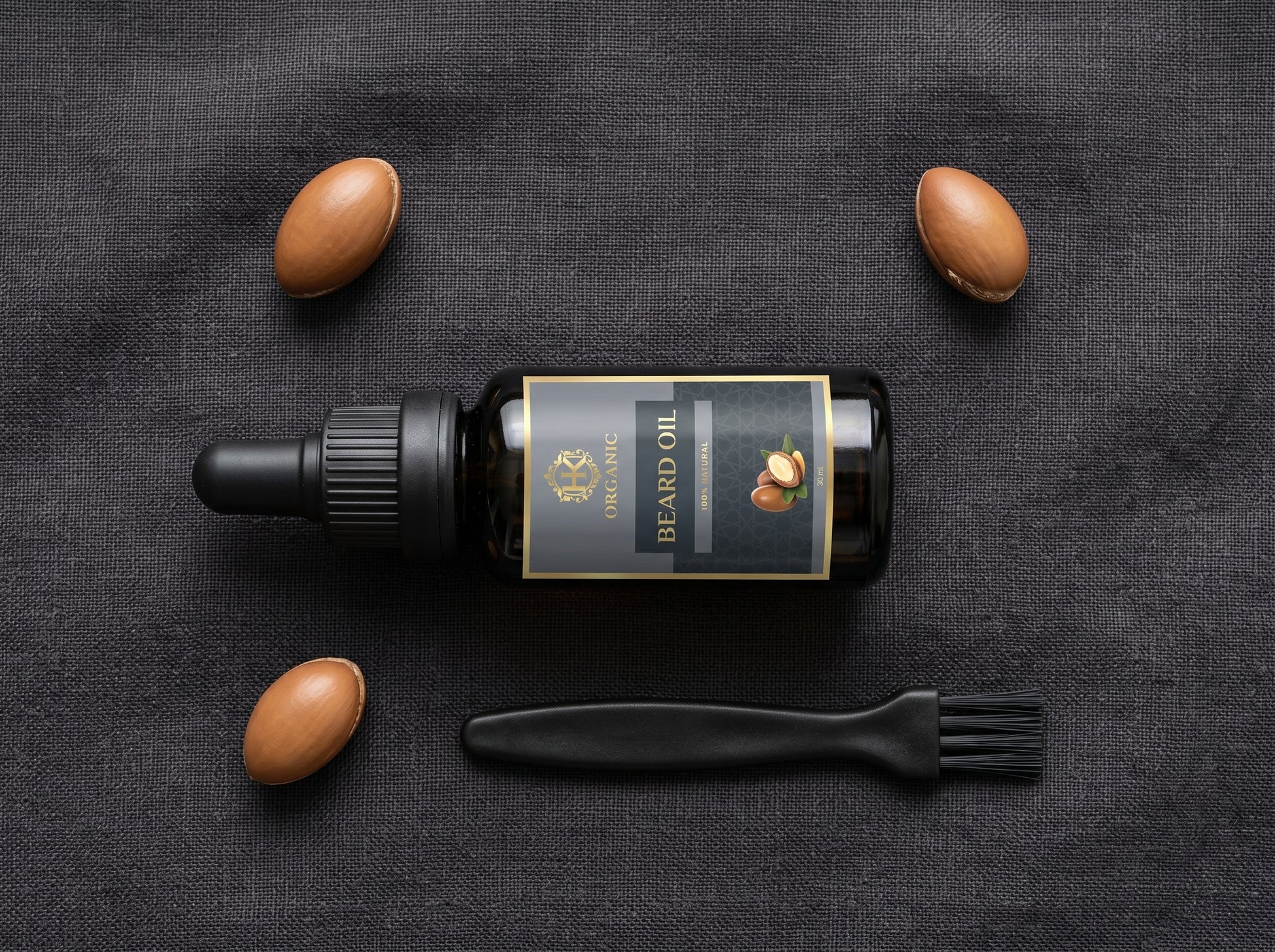 Beard oil bottle with almonds and a brush on a dark fabric background