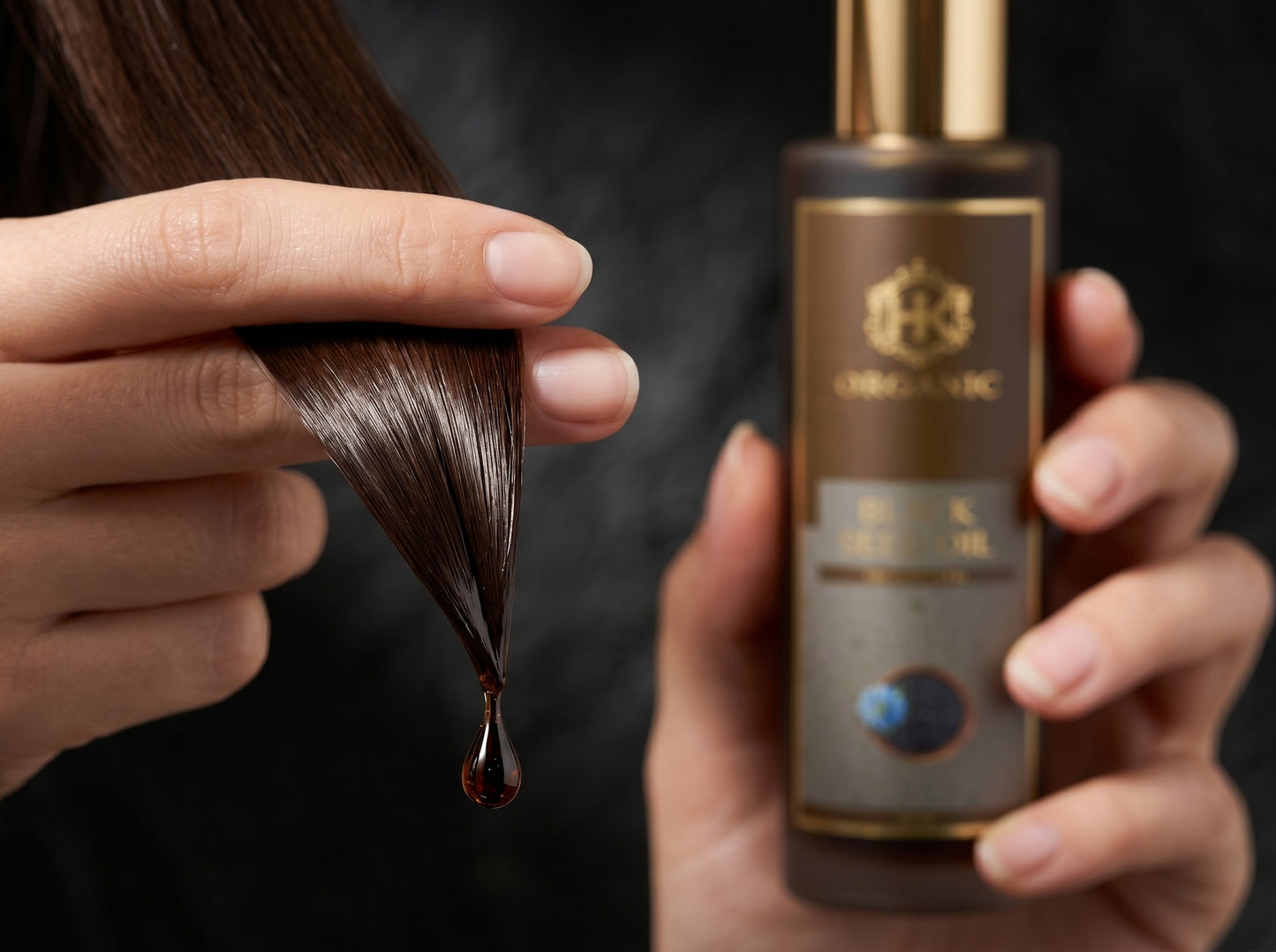 Person holding a bottle of hair oil with a droplet of oil being applied to hair.