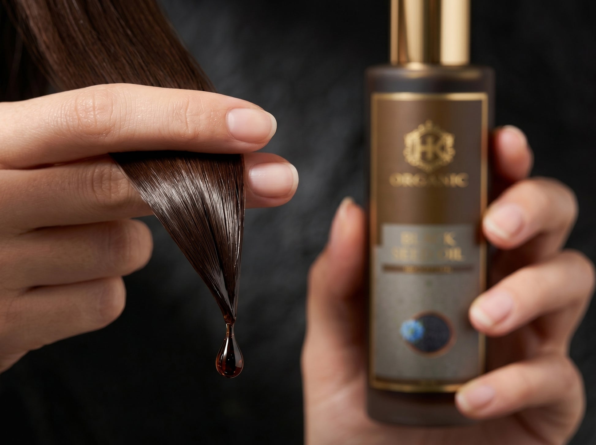 Person holding a bottle of hair oil with a droplet of oil being applied to hair.