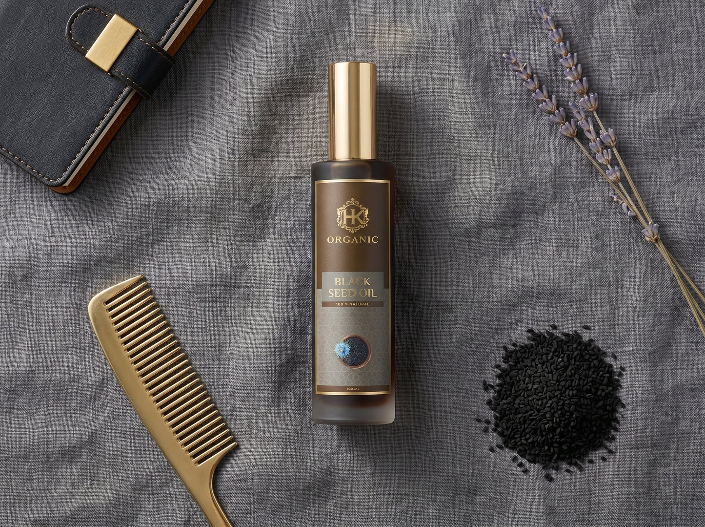 Bottle of organic black seed oil with a comb, seeds, and lavender on a gray fabric background