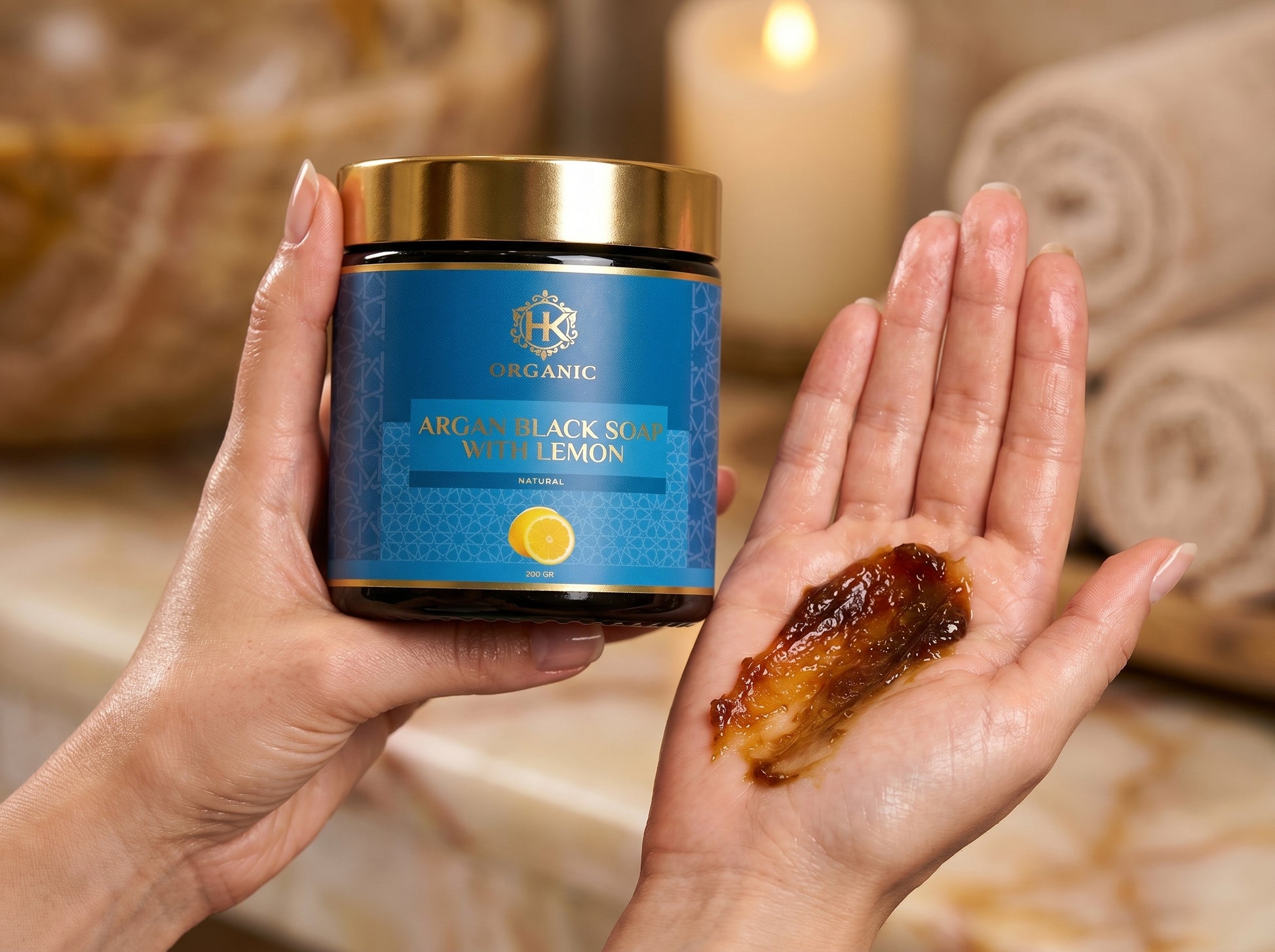 Jar of Argan Black Soap with Lemon held by a hand, showing soap on another hand against a blurred background.