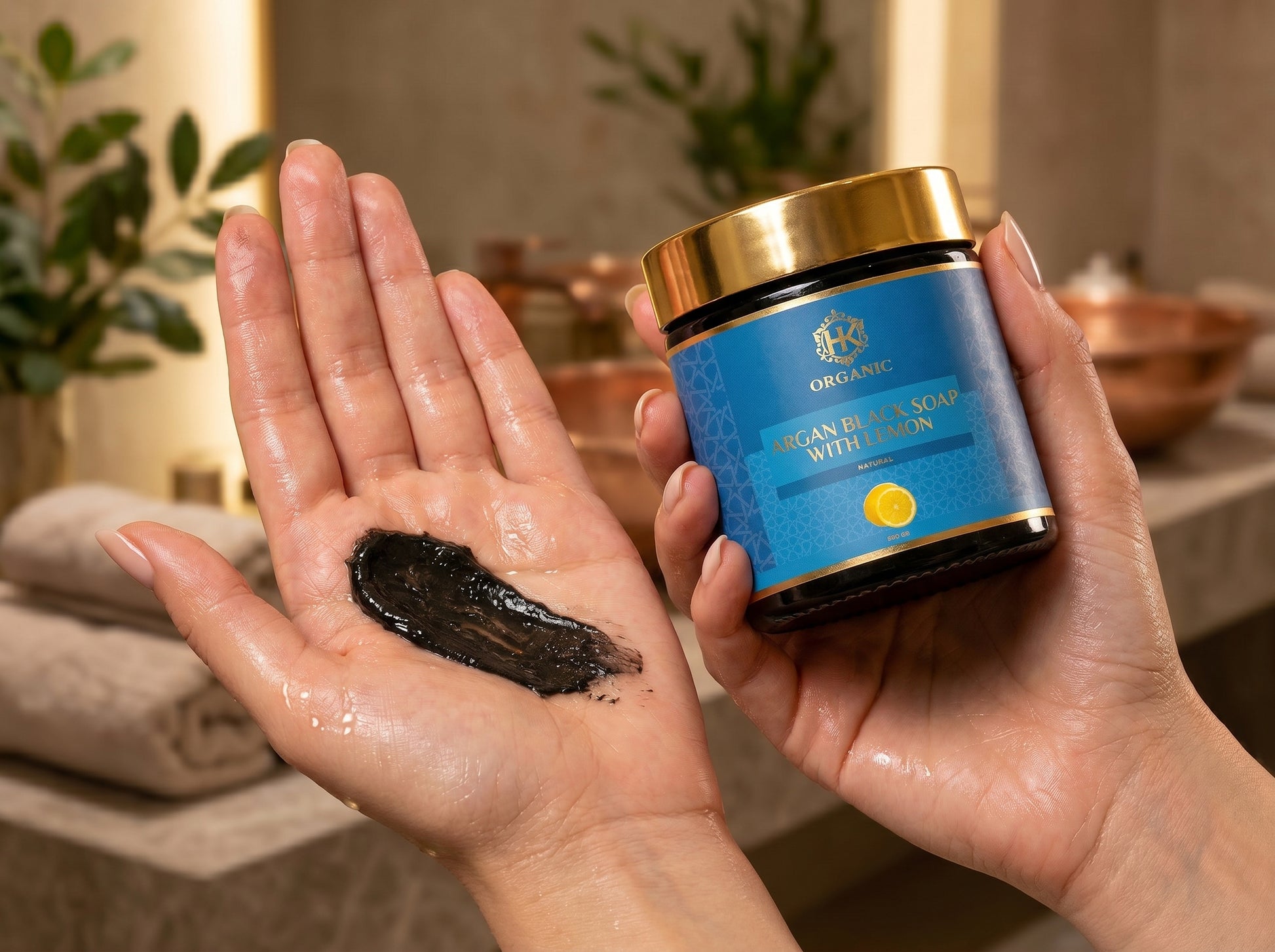 Person holding a jar of organic face scrub and a small amount on their palm in a bathroom setting.