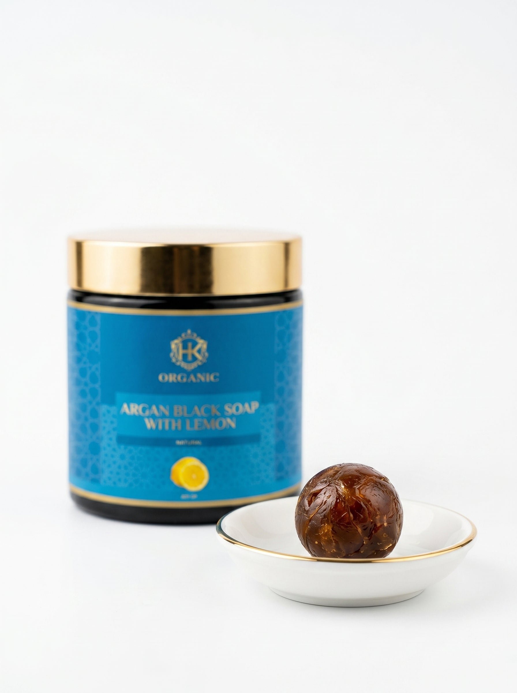 Blue jar of argan black soap with lemon next to a bar of soap on a white plate