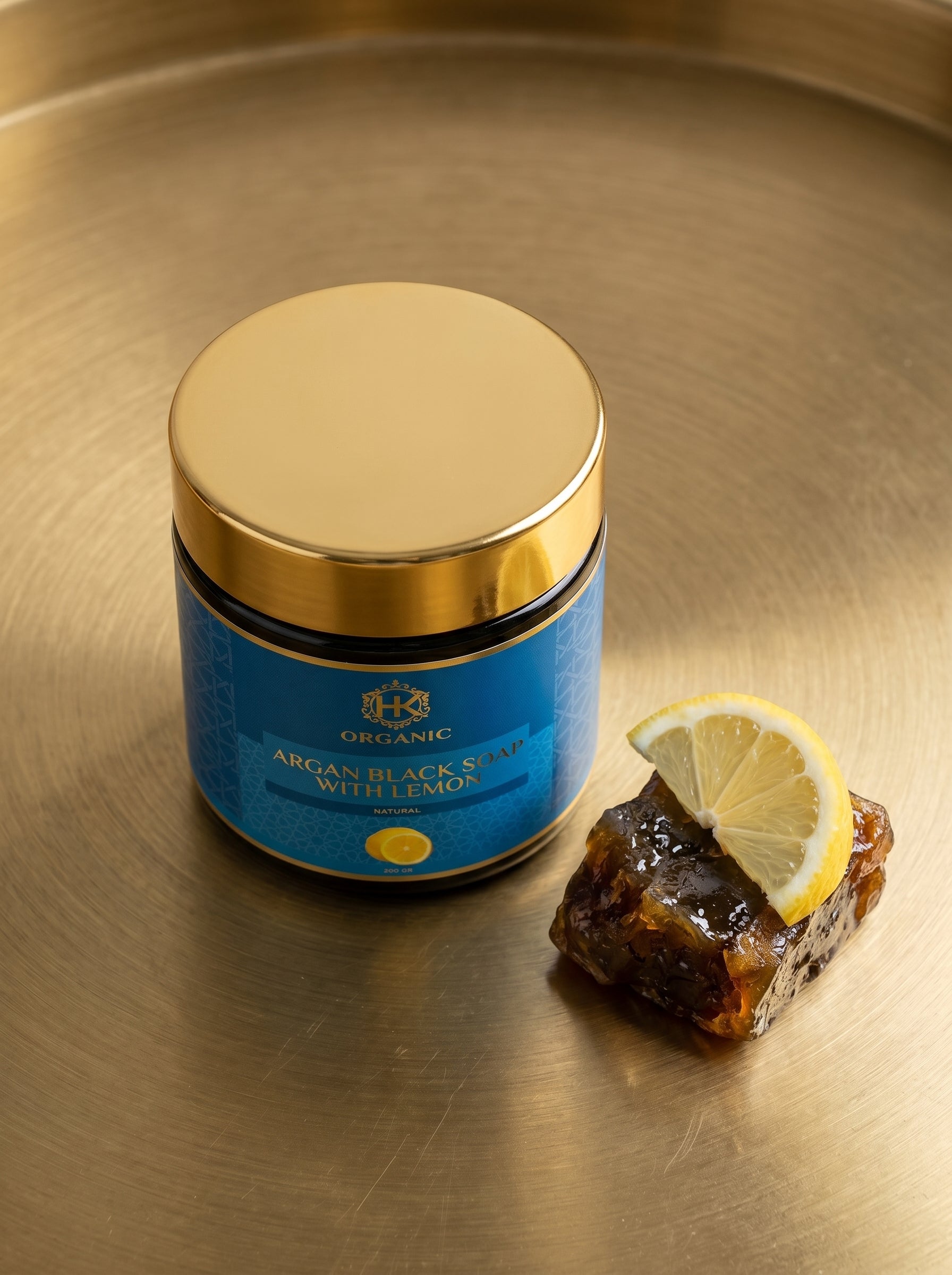 Jar of organic argan black soap with lemon on a gold surface