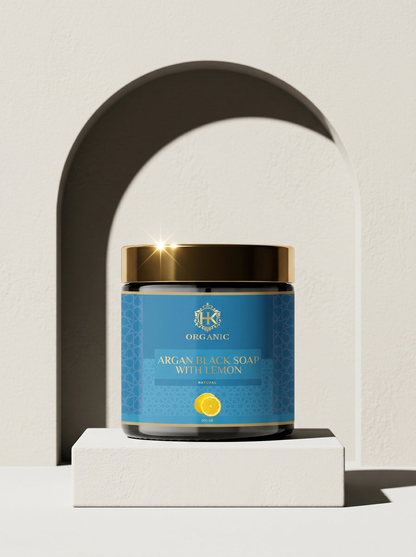 Jar of Argan Black Soap with Golden Highlights on a white platform against a neutral background