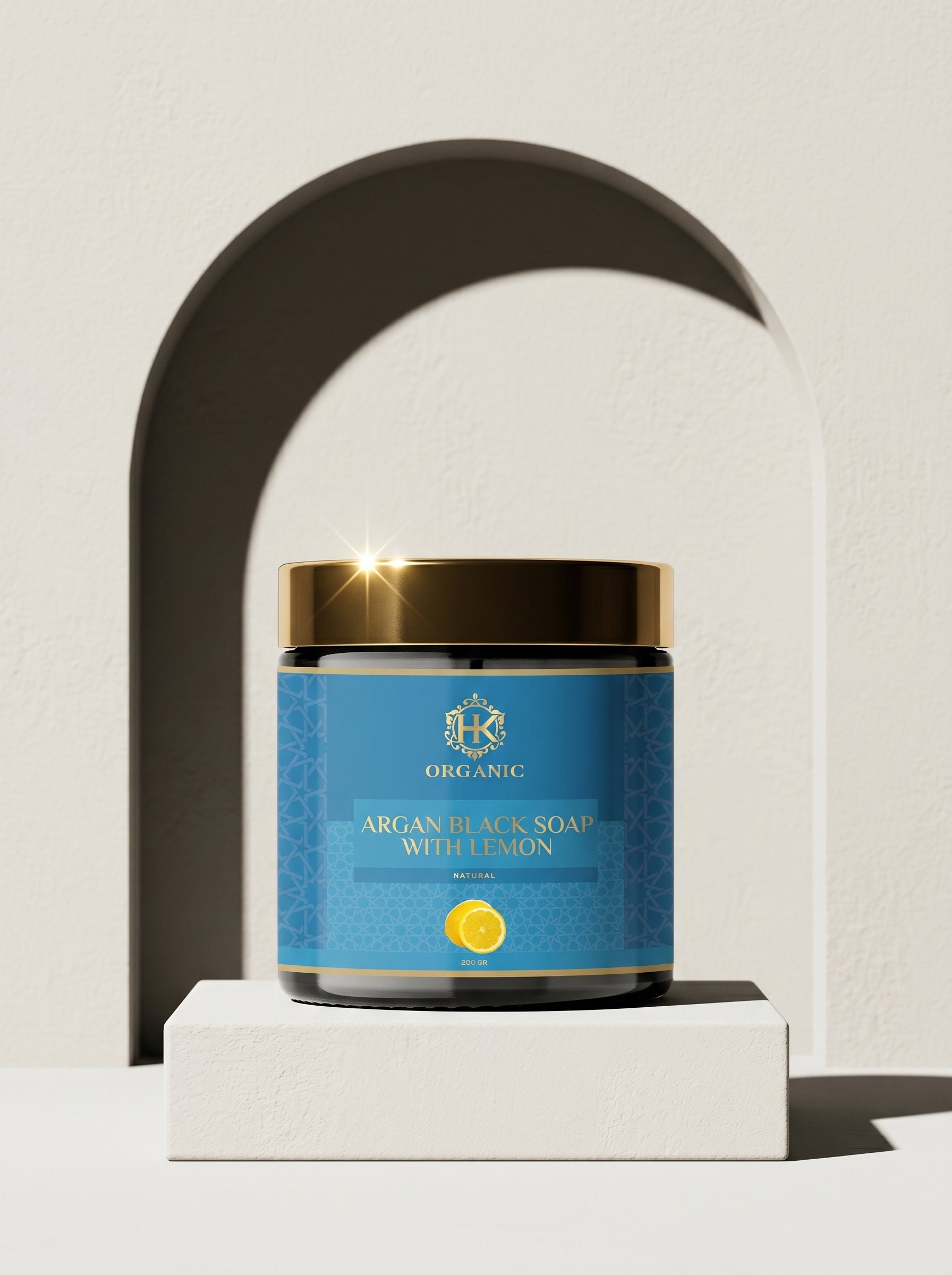 Jar of Argan Black Soap with Golden Highlights on a white platform against a neutral background