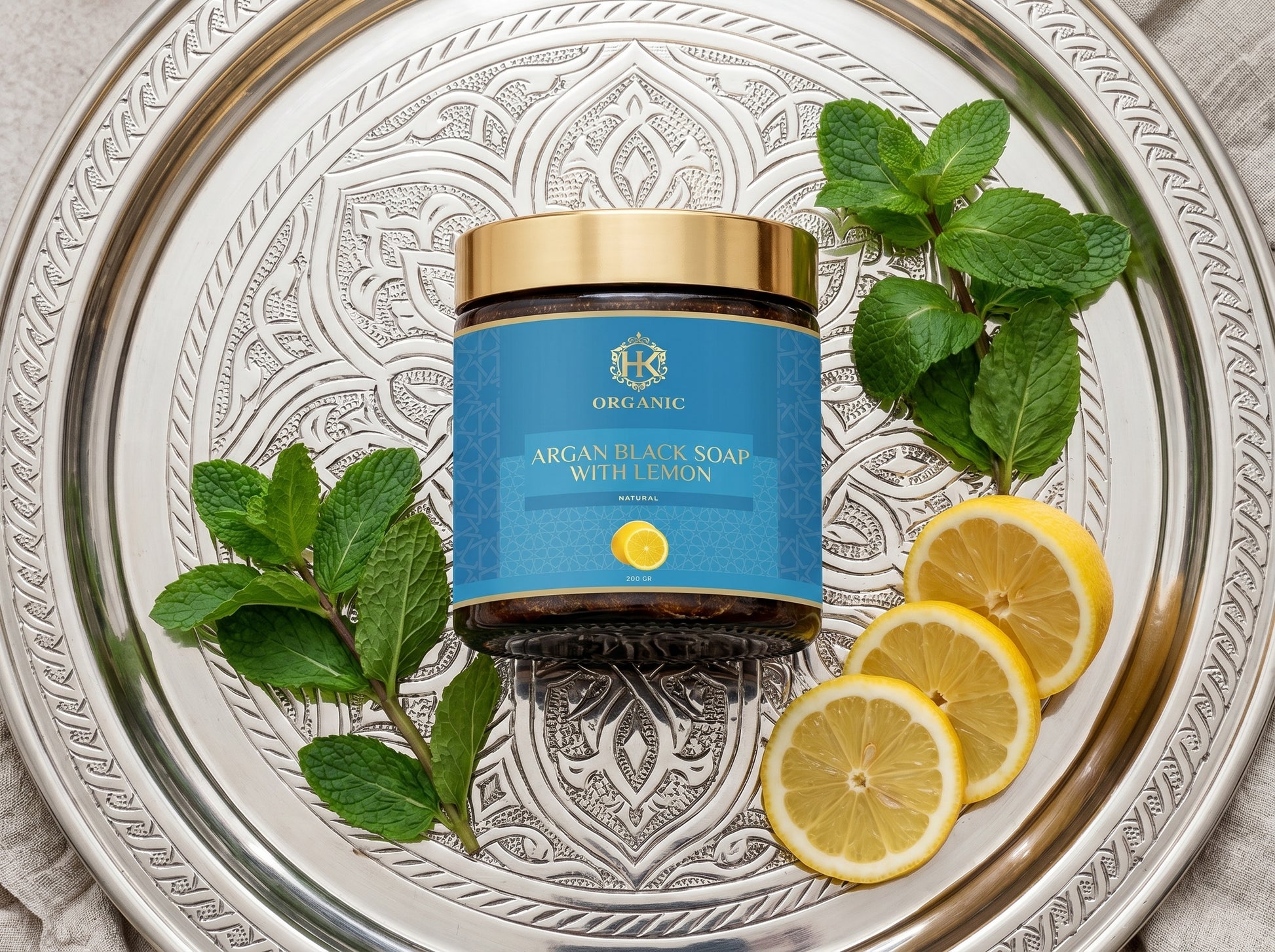 Jar of argan black soap with lemon on a decorative tray with lemons and mint leaves.