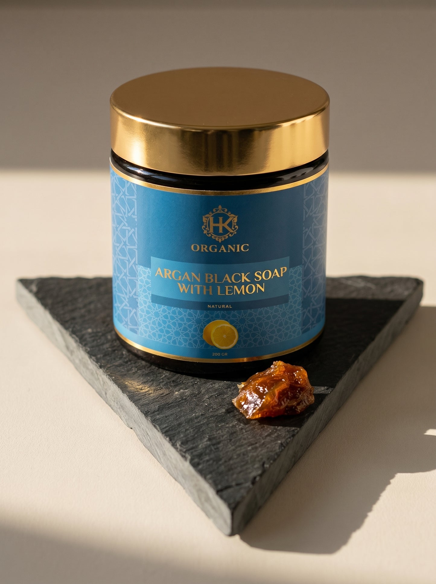 Blue jar of organic argan black soap with lemon on a dark slate stone