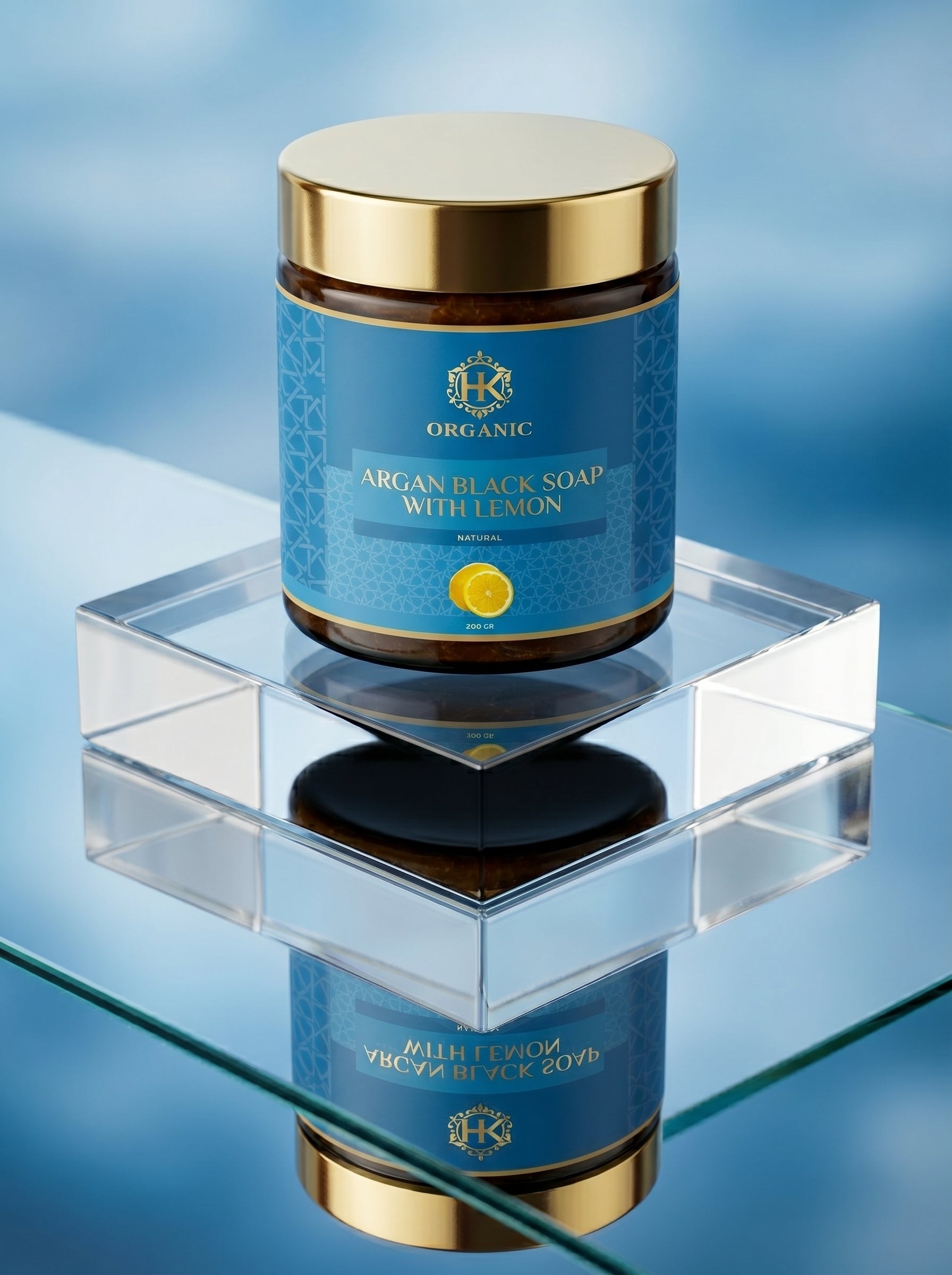 Jar of argan black soap with lemon on a clear stand against a blue gradient background