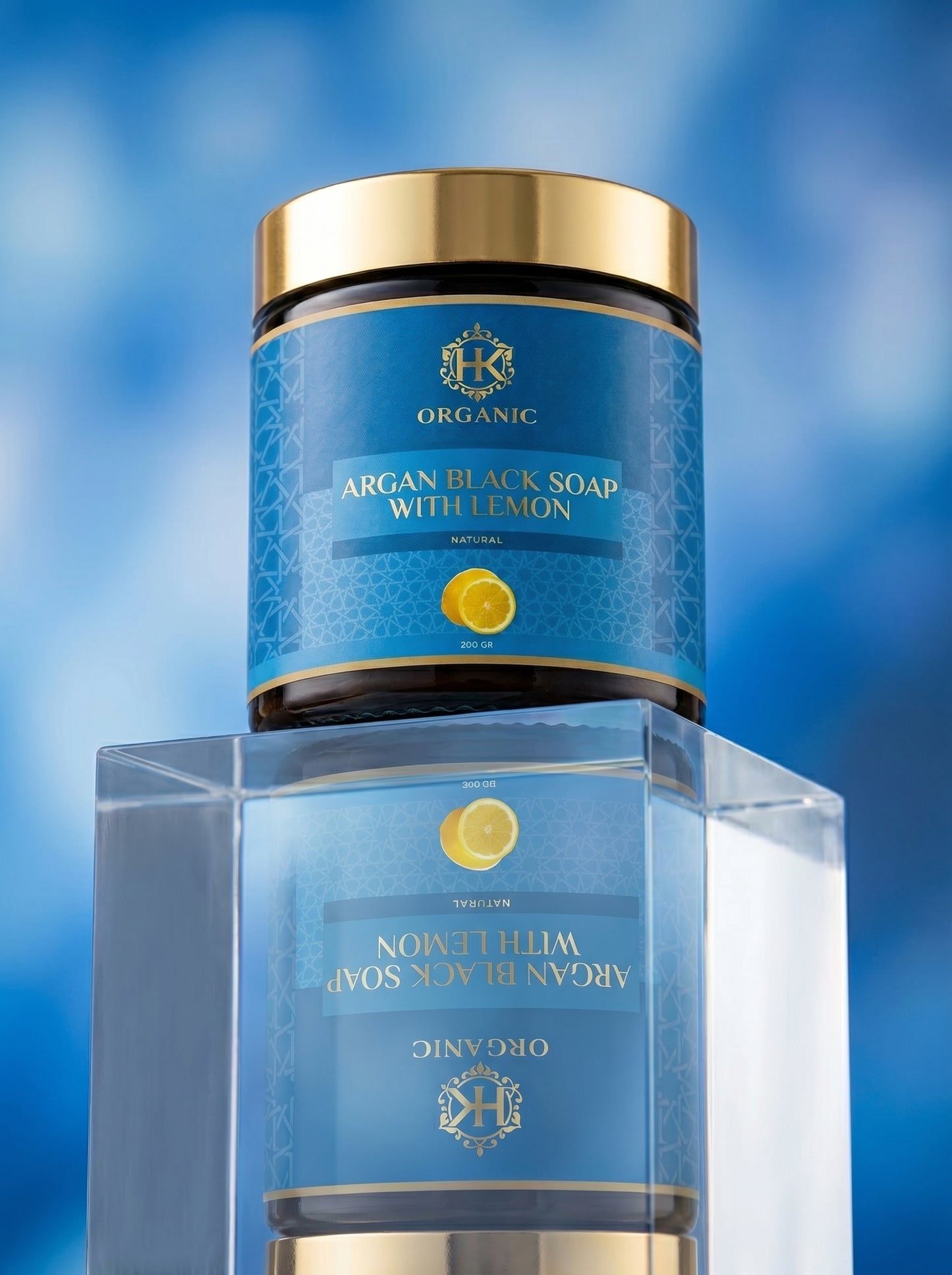 Blue jar of argan black soap with lemon on a clear stand against a blue background