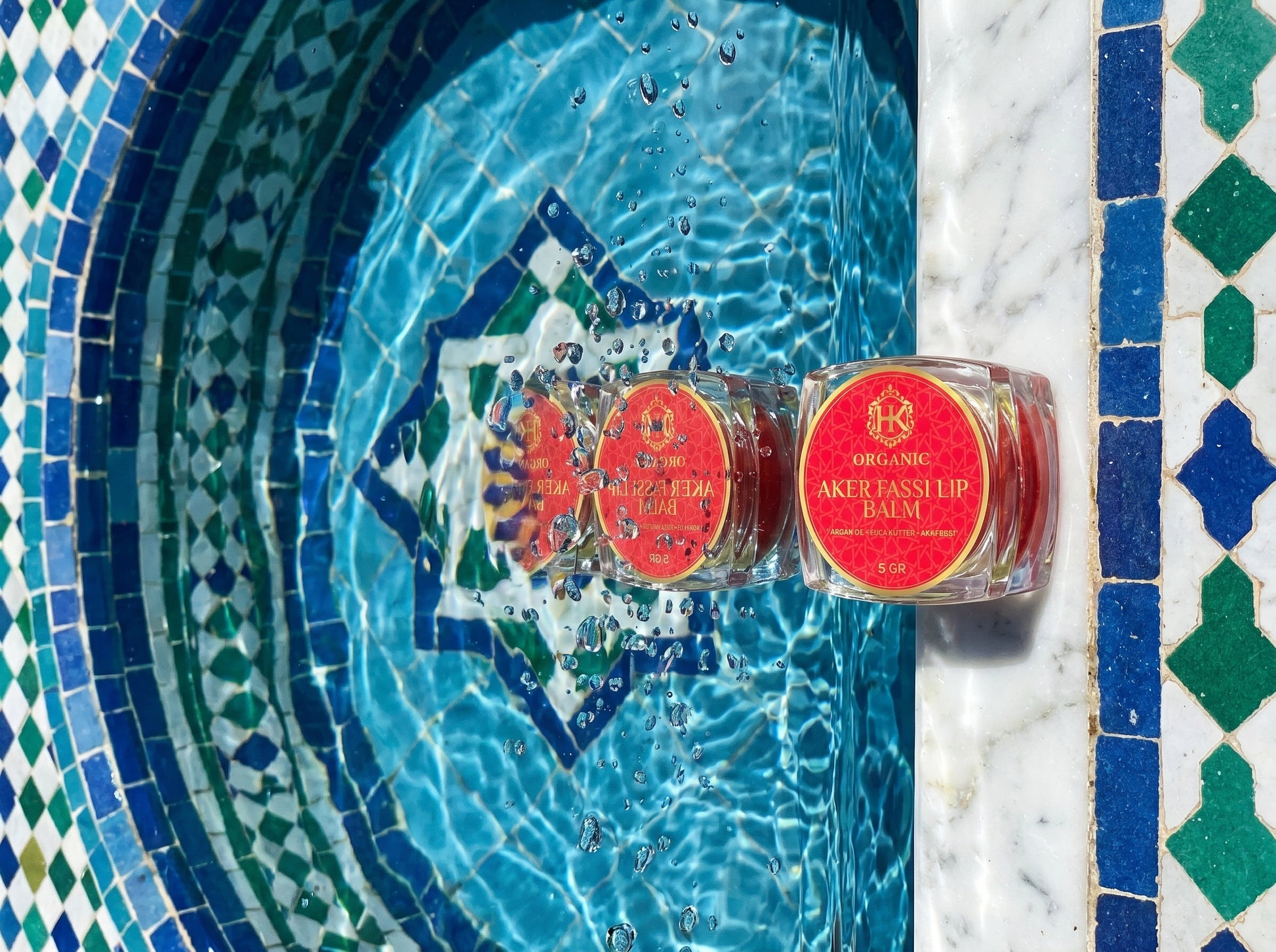 Two lip balm containers with red labels on a mosaic tile background