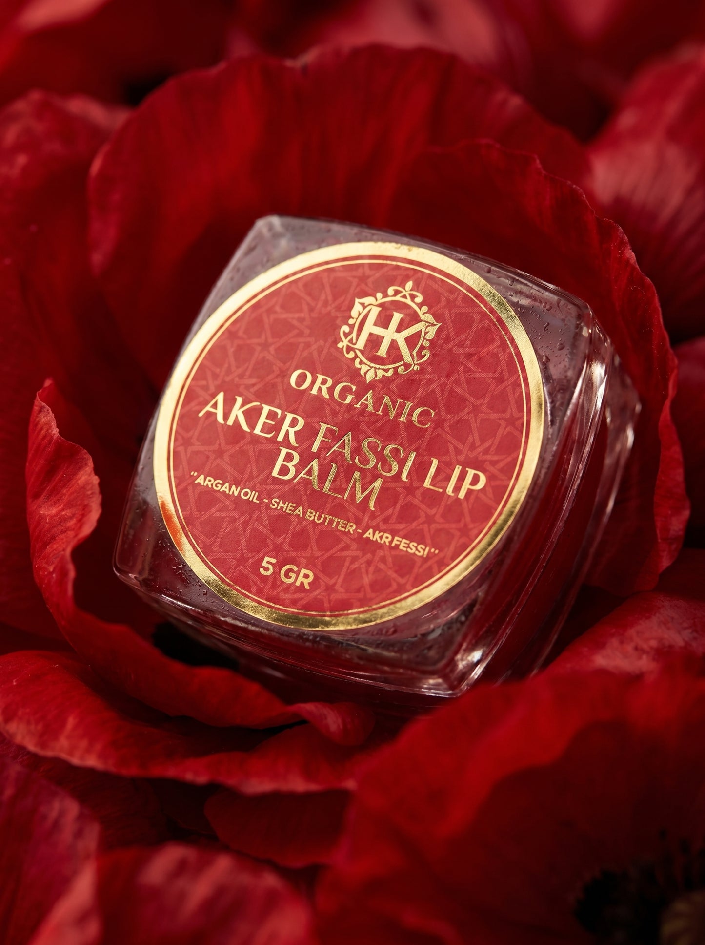 Lip balm container labeled 'Aker Fassi' on red flowers